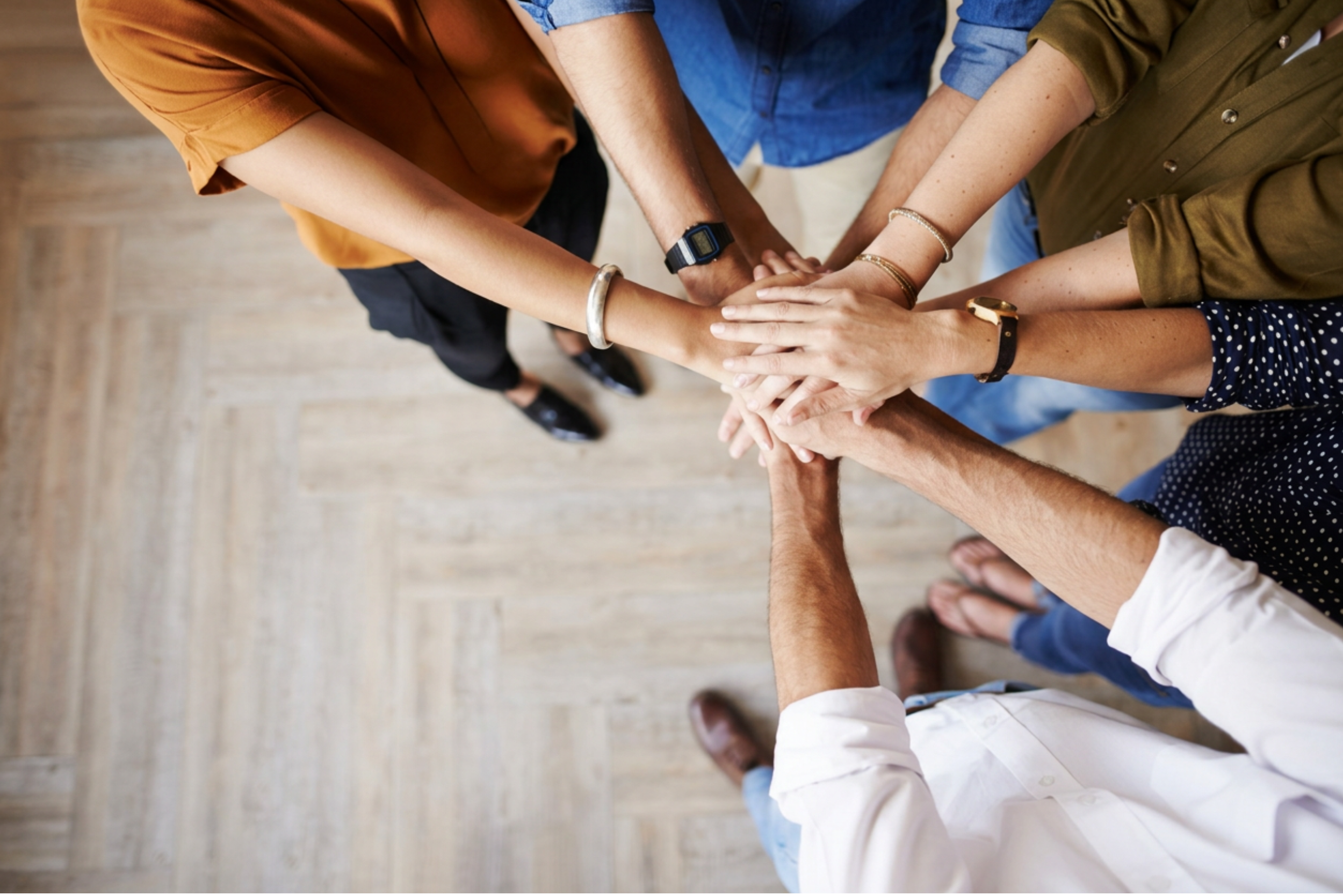 Multiple people standing in a circle, placing their hands together in the center, symbolizing teamwork.