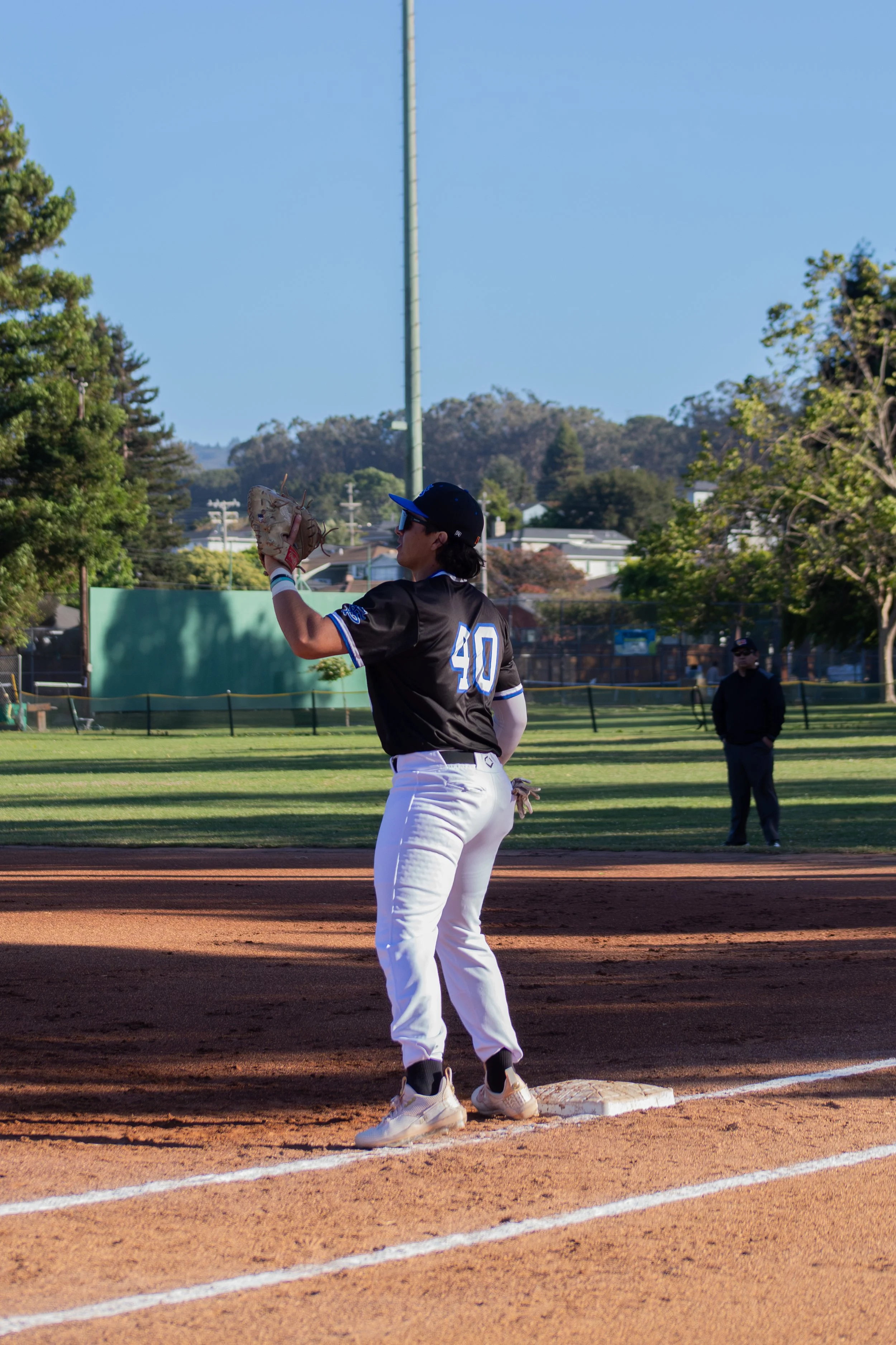 A baseball player standing on a base, preparing to run, wearing a black jersey with the number 40 and white pants on a baseball field during daytime.