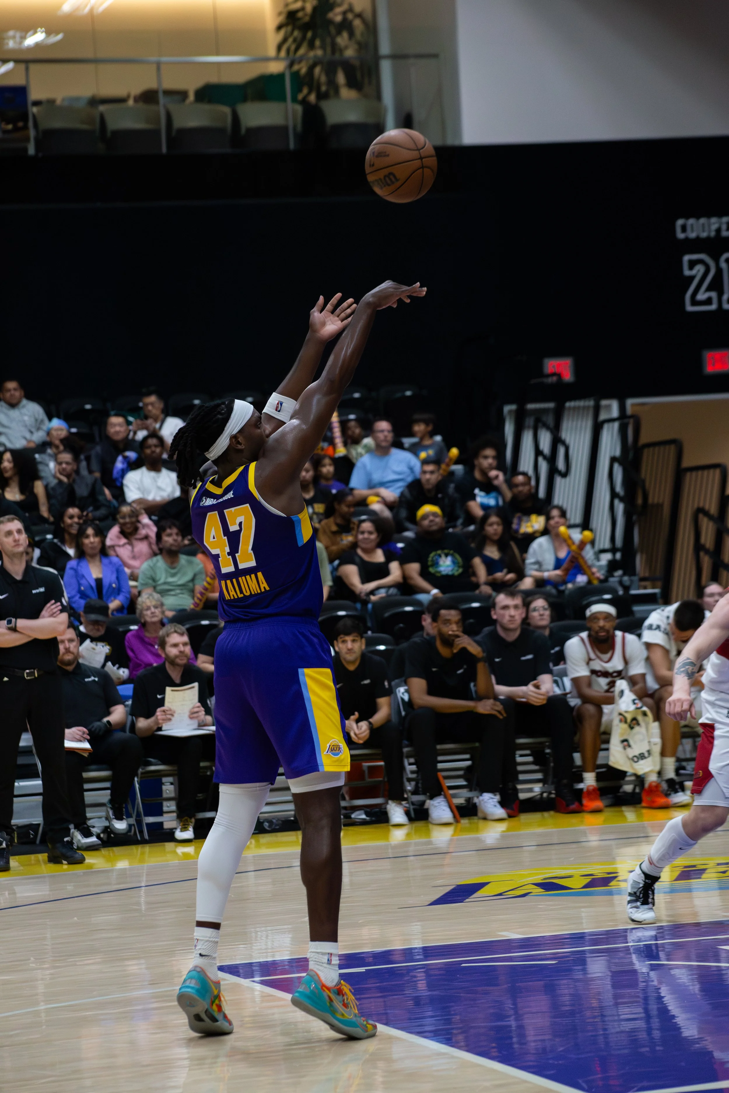 A basketball player wearing a blue and yellow uniform, number 47, shooting a basketball on an indoor court with a crowd watching.