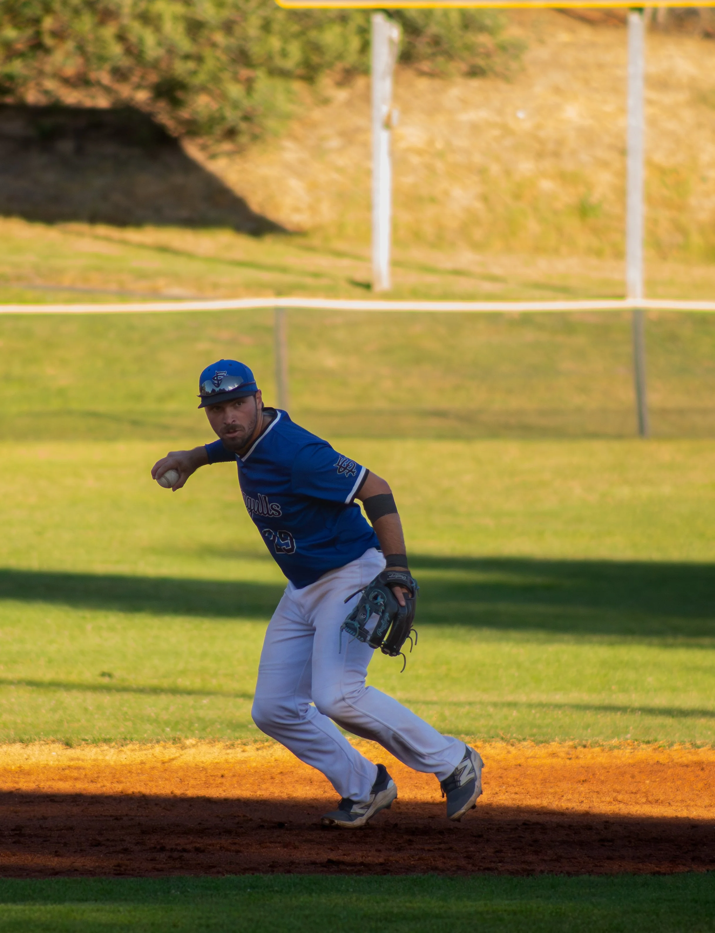 A baseball player in a blue uniform and cap, with the number 29 on his jersey, is running on the field, holding a baseball, during a game at sunset.