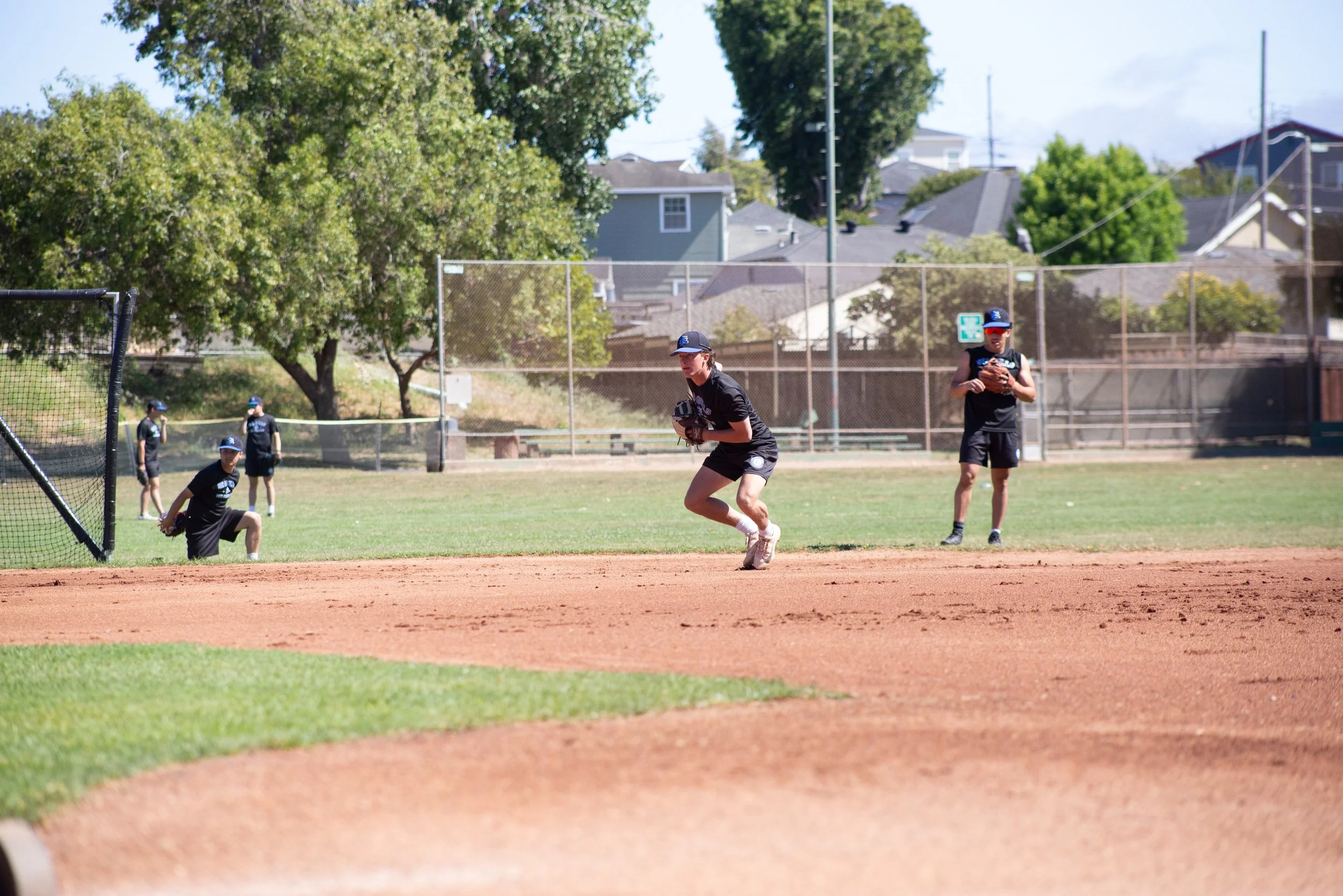 Young boys playing baseball on a field with trees and houses in the background.
