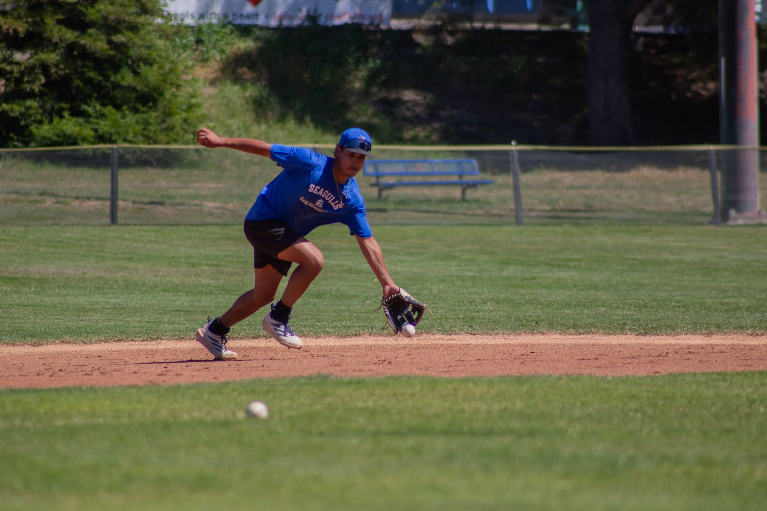 A young baseball player in blue uniform and cap fielding a ground ball on a grassy baseball field.