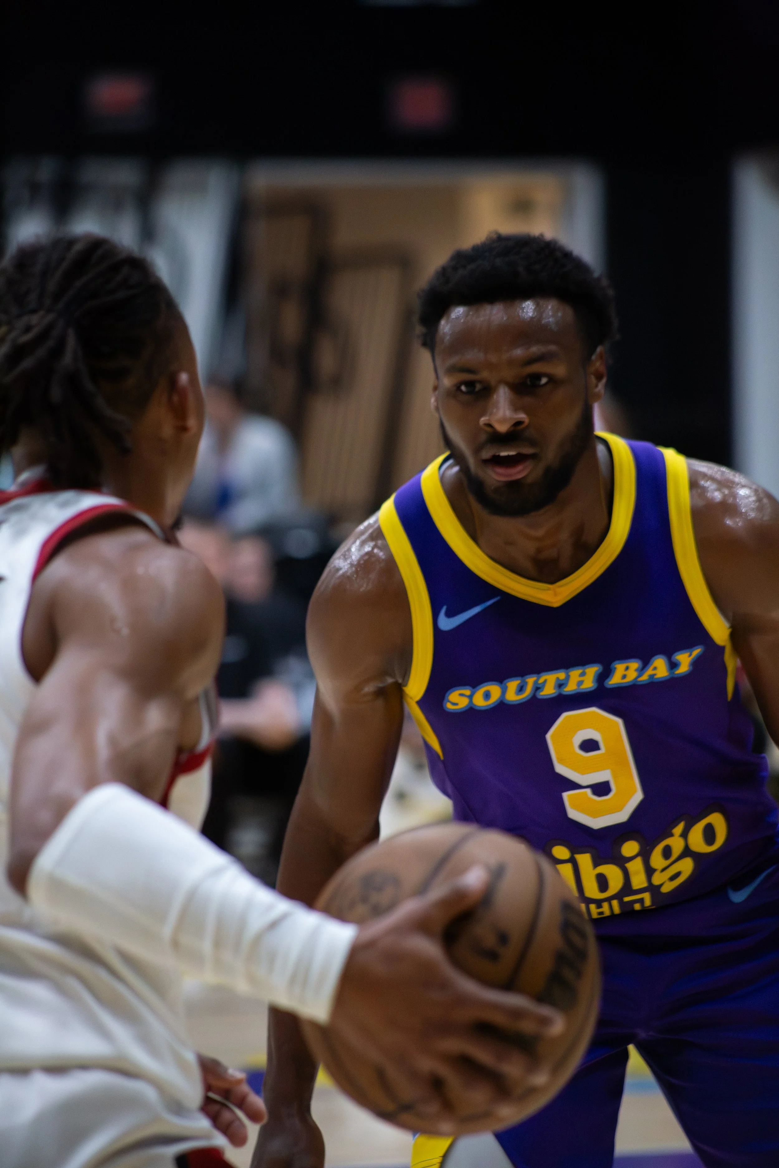 Two basketball players, one in a white uniform and one in a blue uniform with yellow accents, competing for possession of a basketball during a game. The player in blue has 