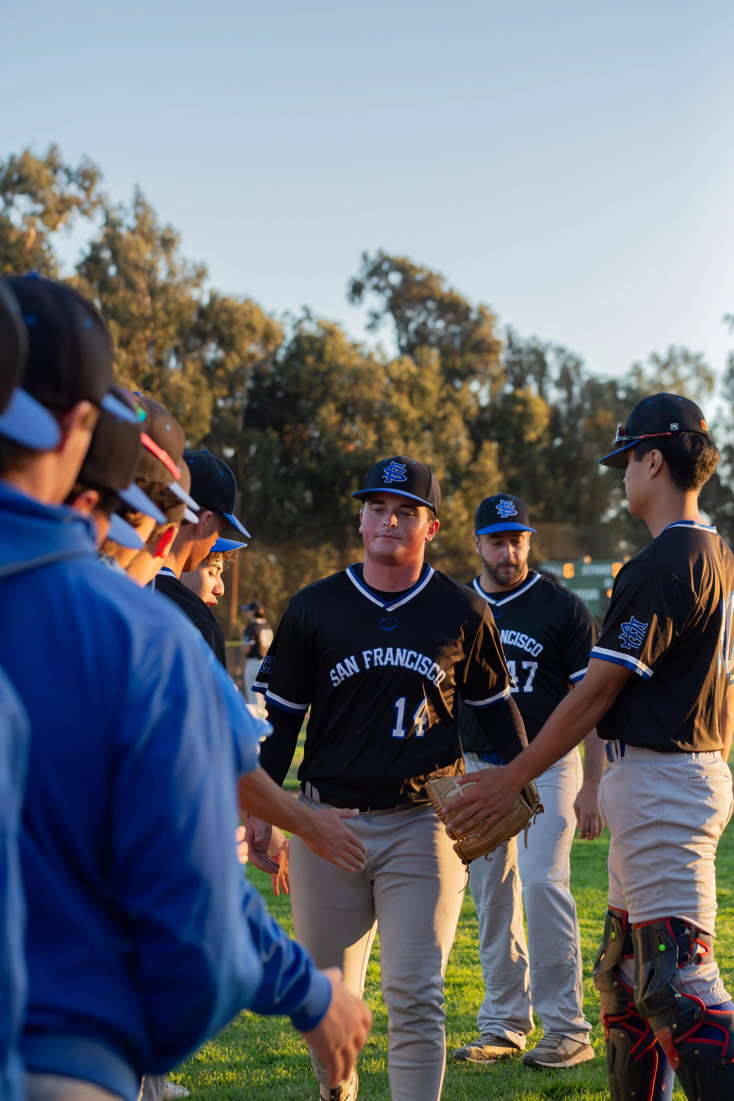 A group of baseball players from San Francisco huddle with hands together on the field during sunset.