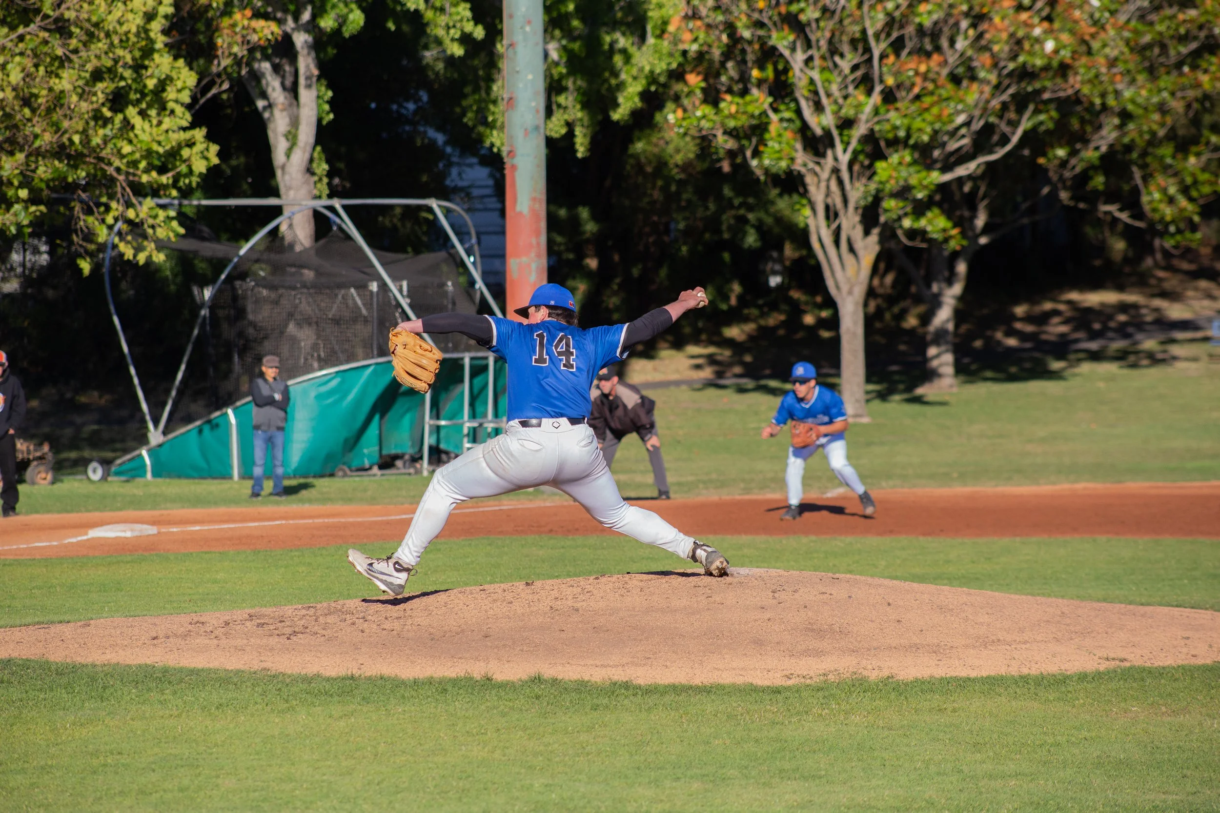 A baseball player wearing a blue jersey with the number 14 is pitching from the mound during a game on a baseball field.