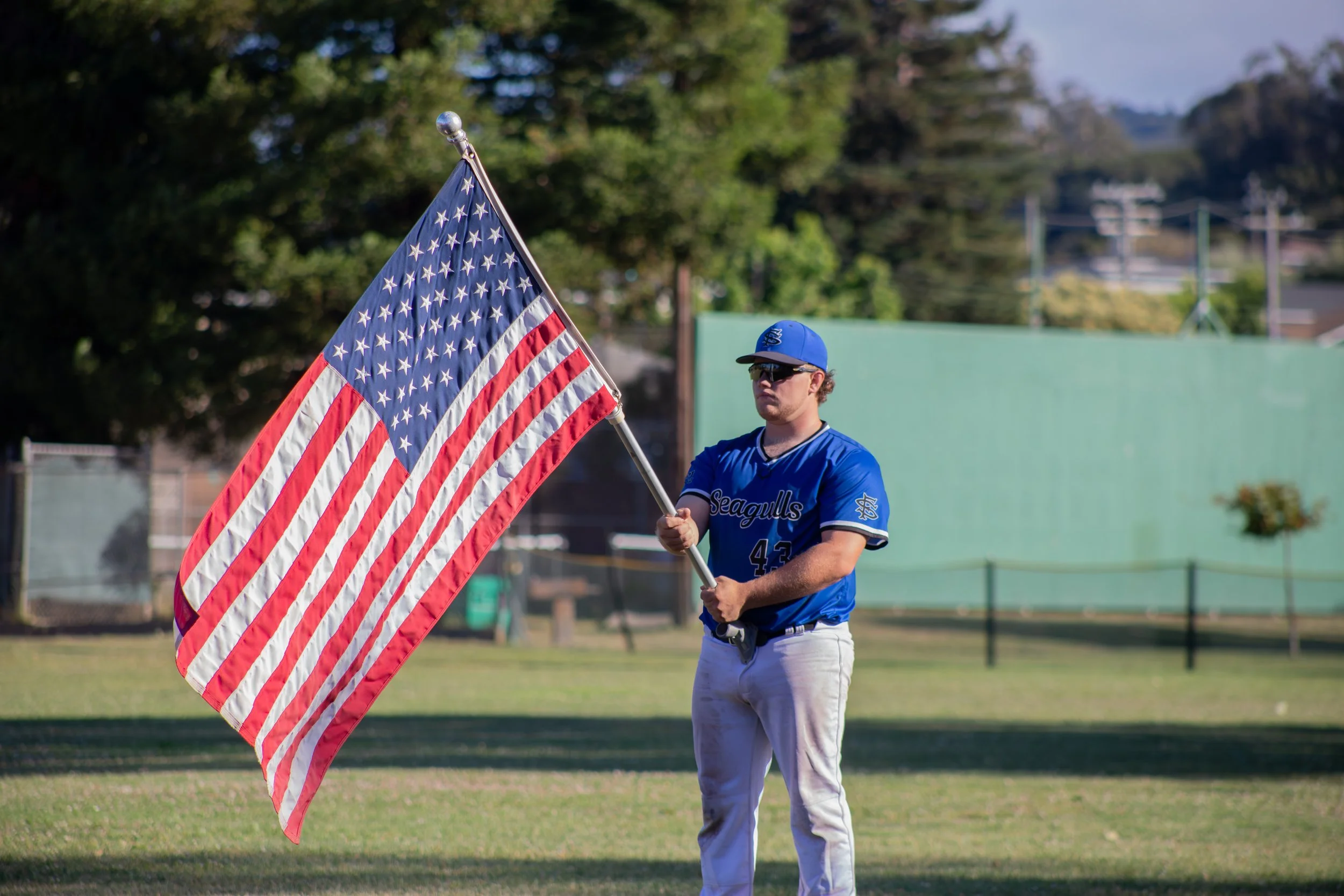 A baseball player holding an American flag on a baseball field.
