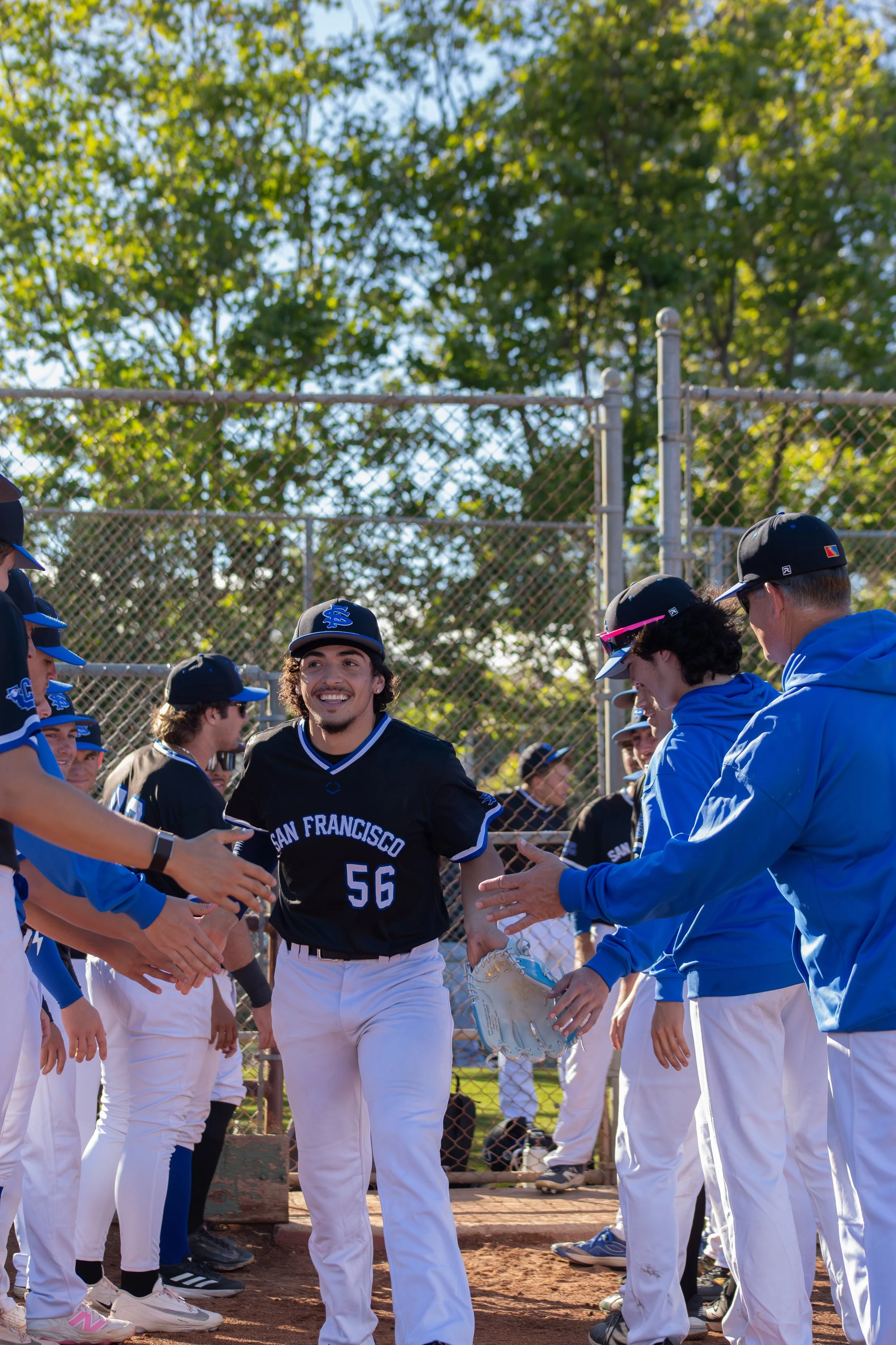 A baseball player in a black uniform with 'San Francisco' and the number 56 is smiling and shaking hands with people dressed in blue and black uniforms at a baseball field during daytime.