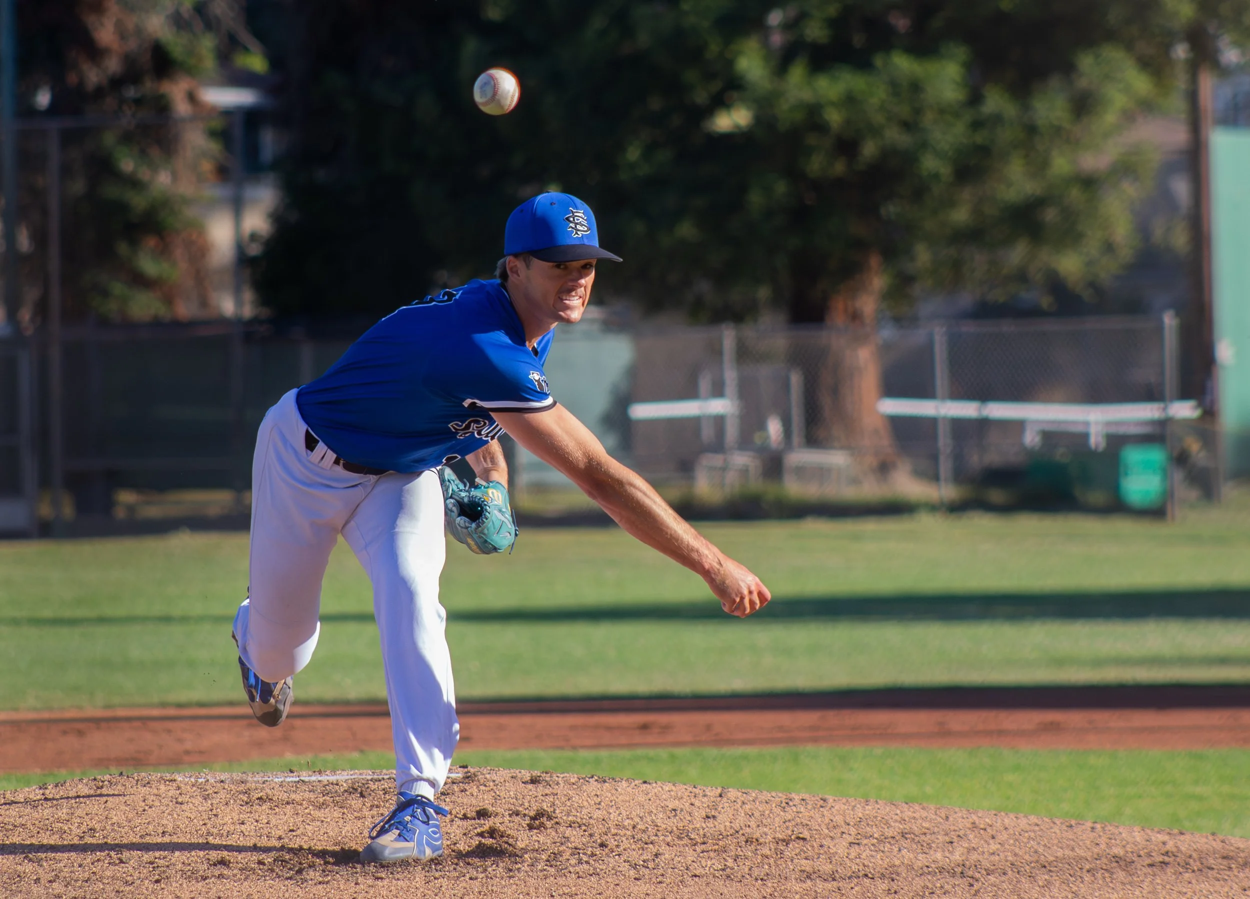 A baseball player in a blue uniform and cap pitching on a baseball field.