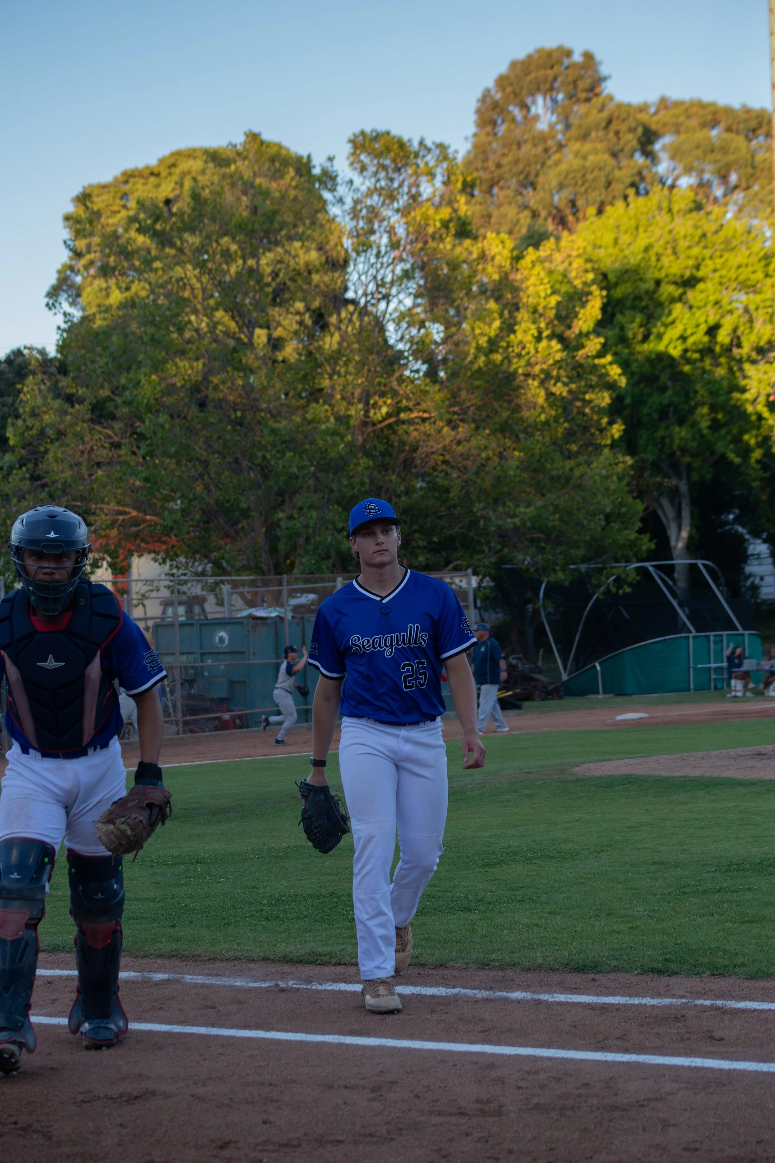 Baseball players walking on the field after a game, with trees and a blue sky in the background.