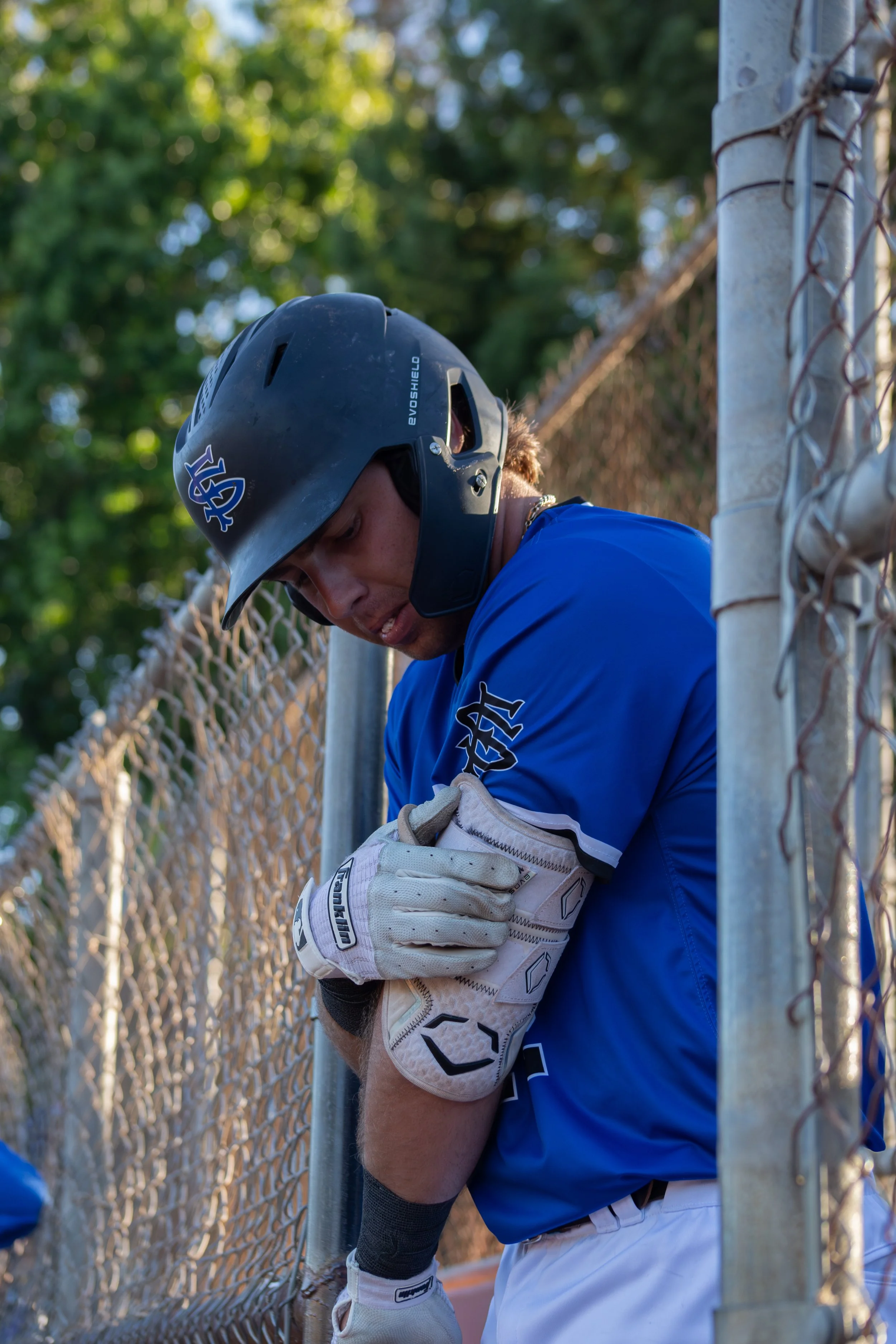 A baseball player in a blue uniform and black helmet leaning against a chain-link fence on a baseball field.