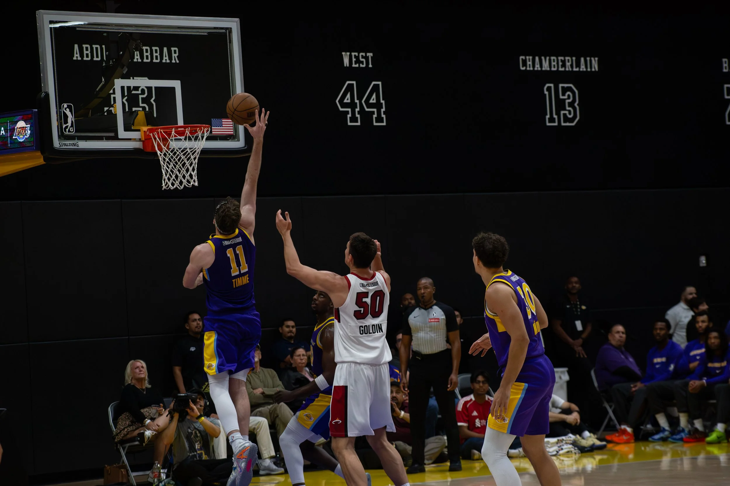 A basketball player in a yellow and blue jersey jumping to make a shot near the basket as opposing players and fans look on.