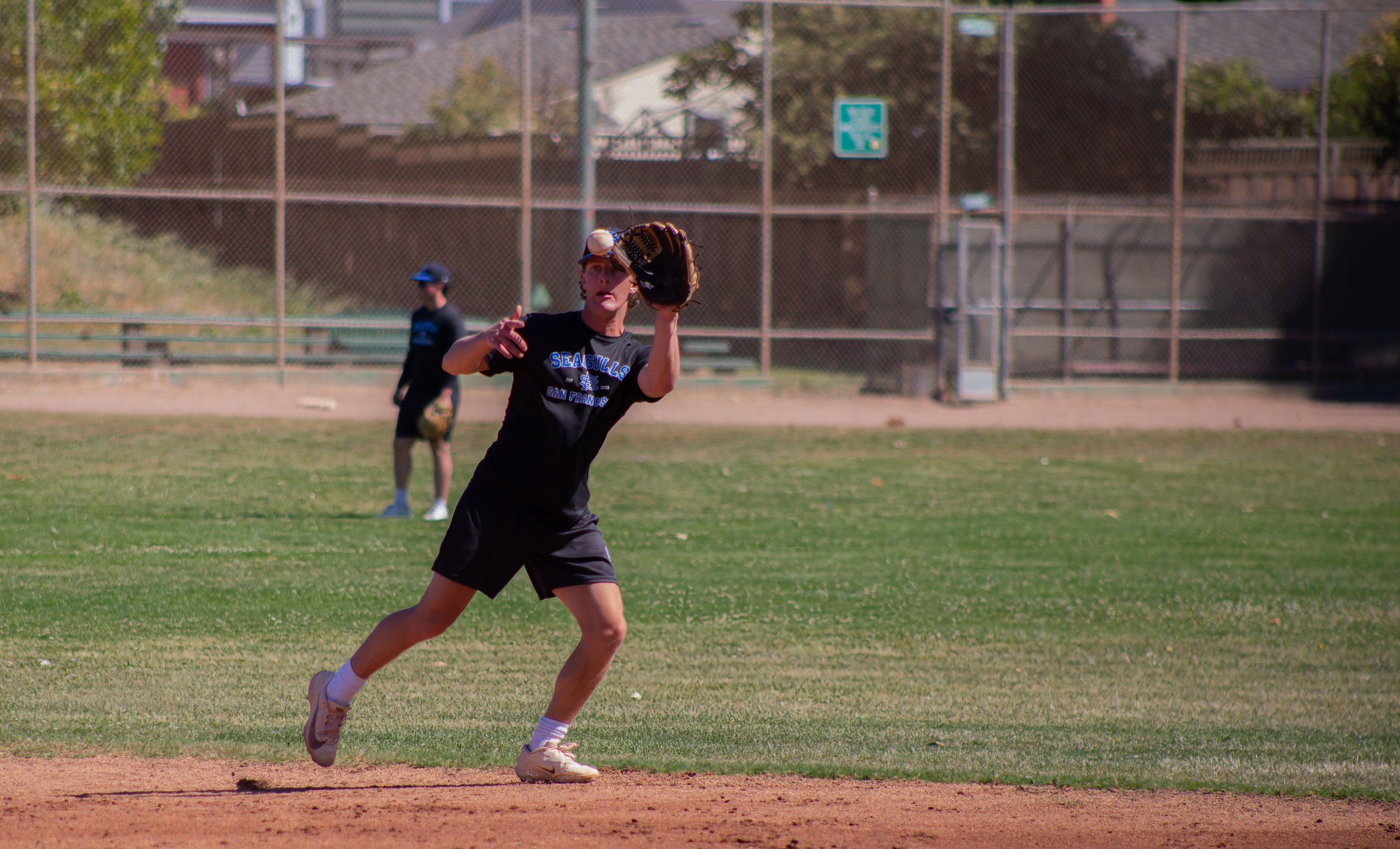 A young girl playing baseball on a field, wearing a black T-shirt, shorts, and a baseball glove, with a bright and sunny background.