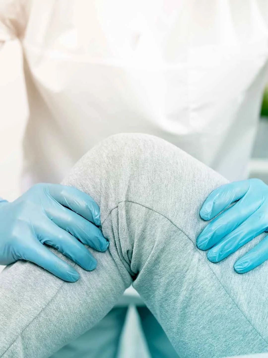 Mano con guantes azules sosteniendo una rodilla con dolor.
