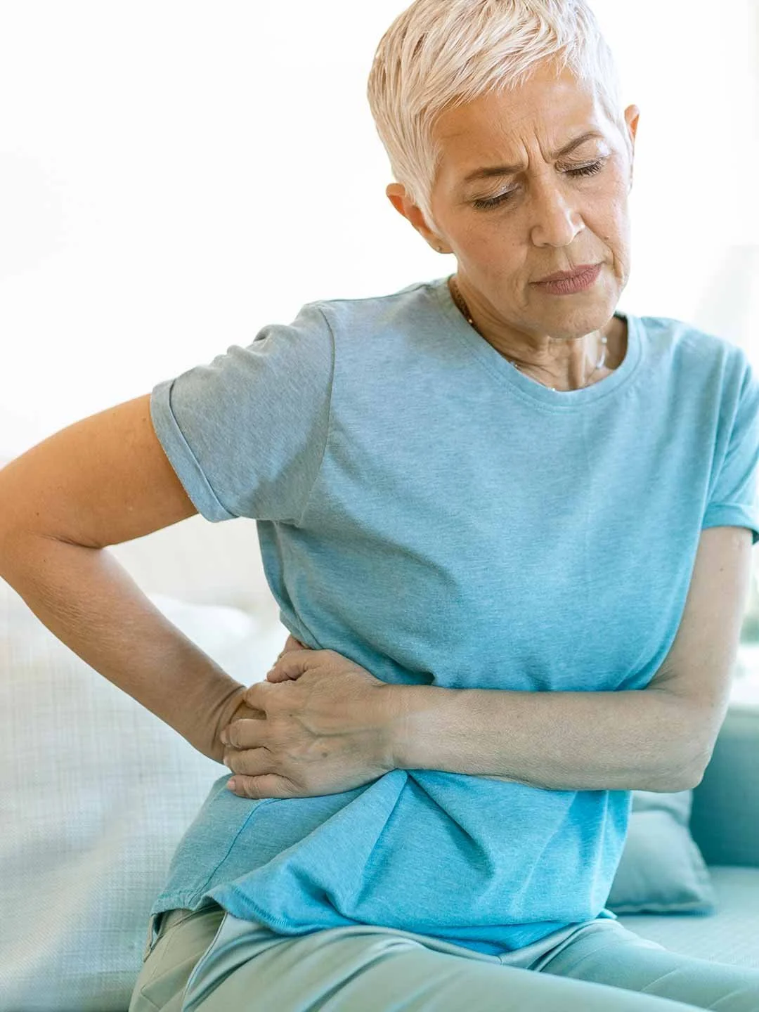 Mujer mayor con dolor de estómago, sosteniéndose el abdomen con expresión de malestar.