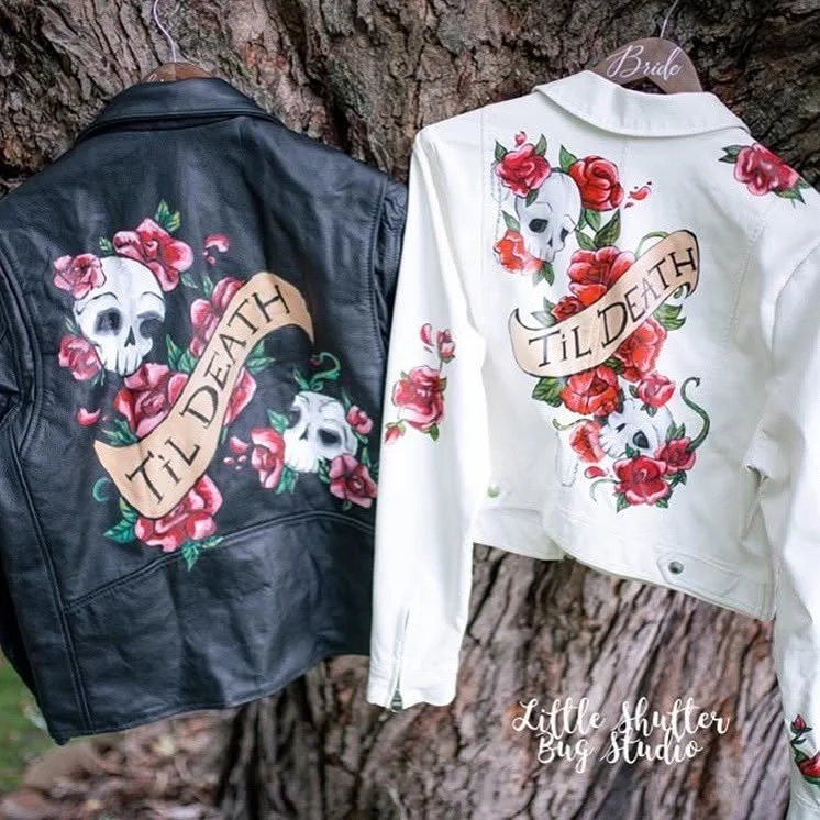 Black and white leather jackets hanging on a tree, both with a skull surrounded by pink roses and a ribbon with the text 'Til Death'. The white jacket has a 'Bride' tag, and the studio's name 'Little Shutter Bug Studio' is at the bottom.