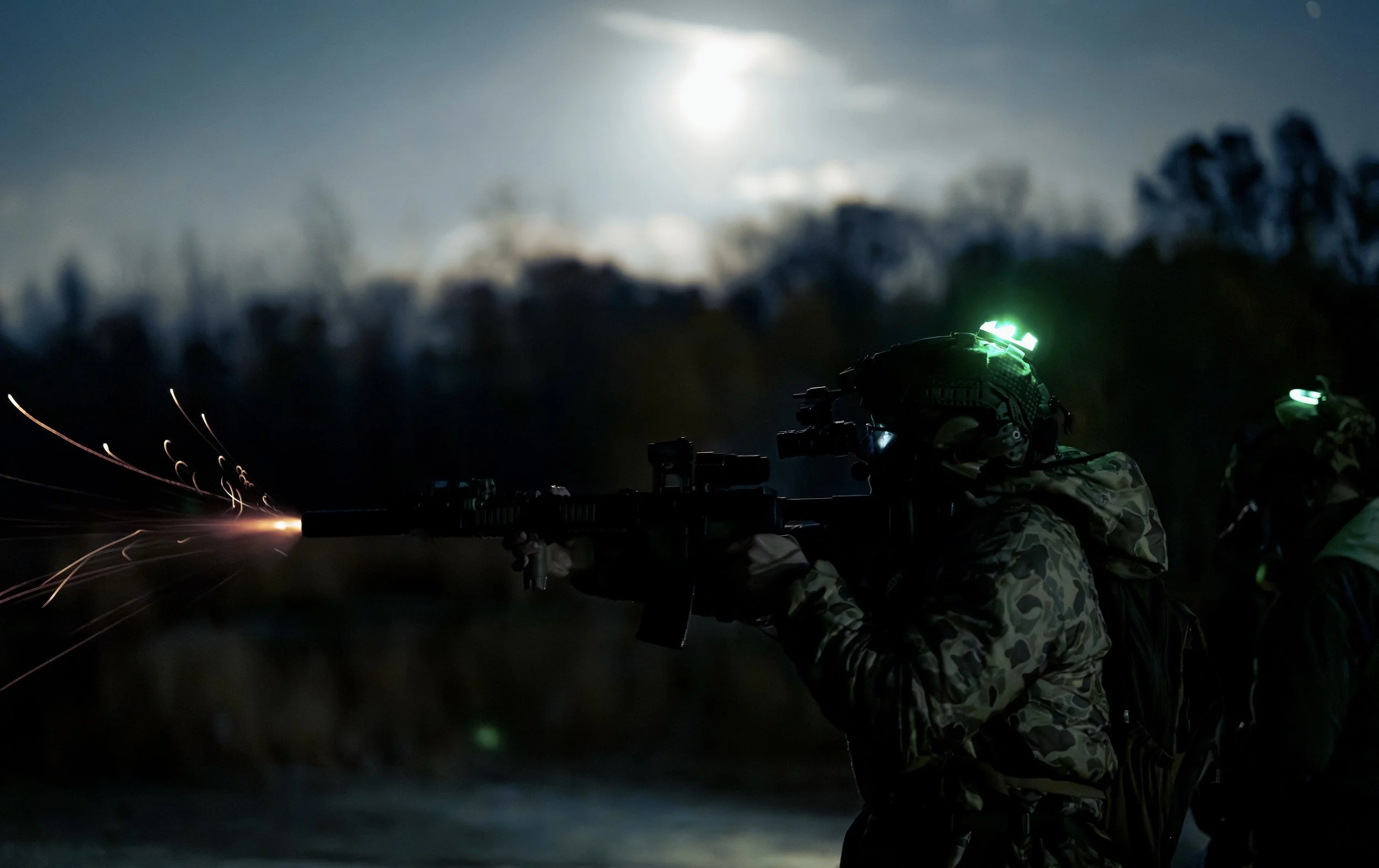 Two soldiers in camouflage uniforms firing a machine gun during nighttime operation, with nearby sparks and a bright full moon in the cloudy sky.