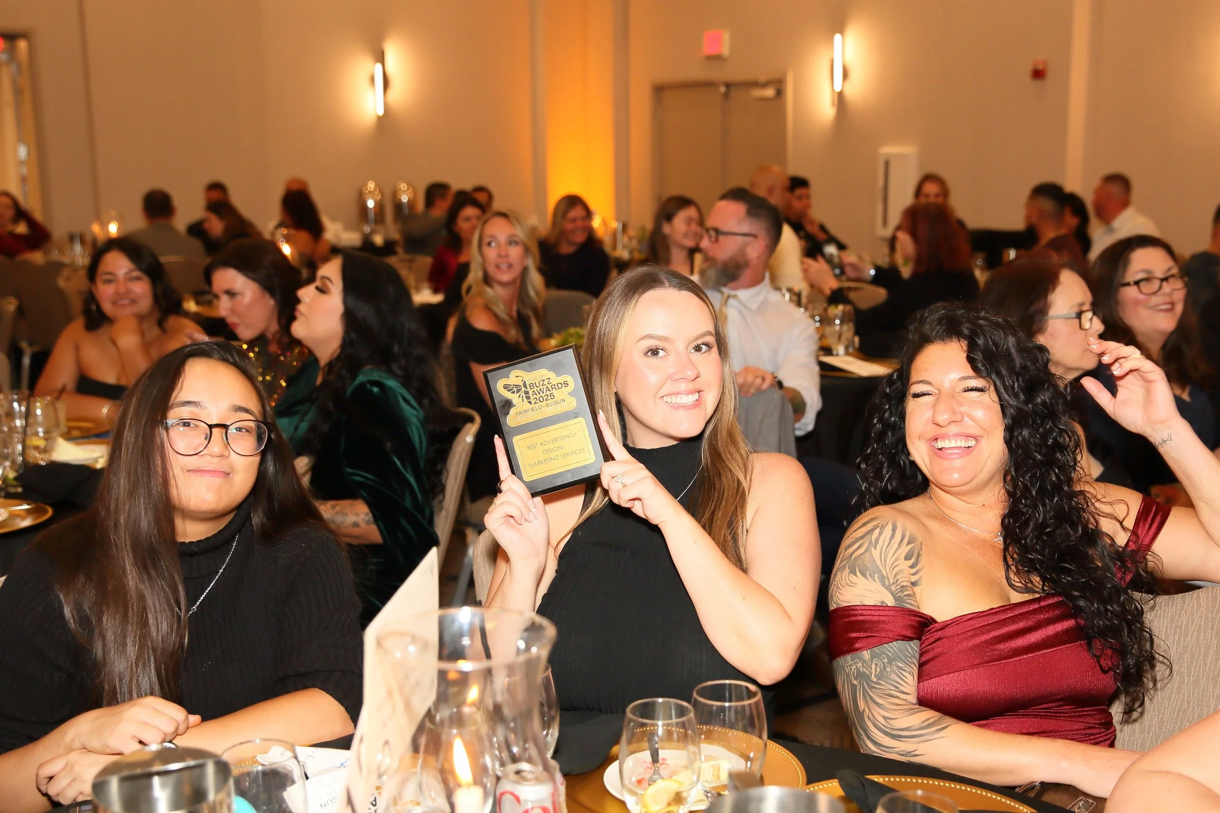 Group of people at an awards ceremony, celebrating and smiling, with a woman in the center holding a plaque.