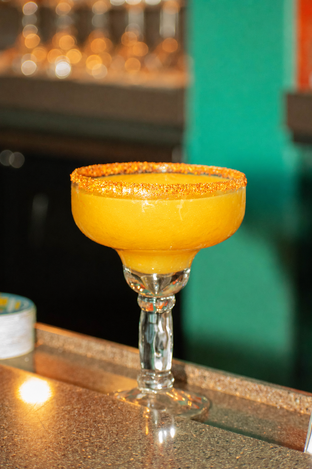 Yellow cocktail in a glass with a salted rim, placed on a bar countertop.