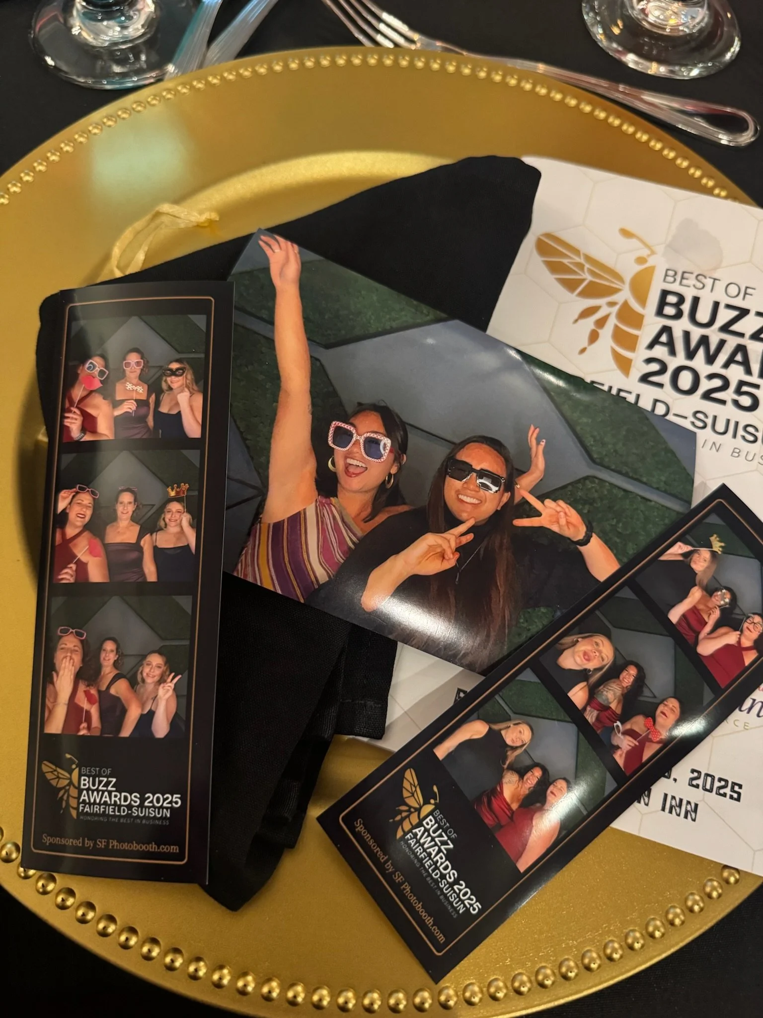 Photo of photo booth strips and a brochure for the 2025 Buzz Awards at Fairfield-Suisun, with images of people in fun costumes and accessories at the event, placed on a golden tray with beaded rim.
