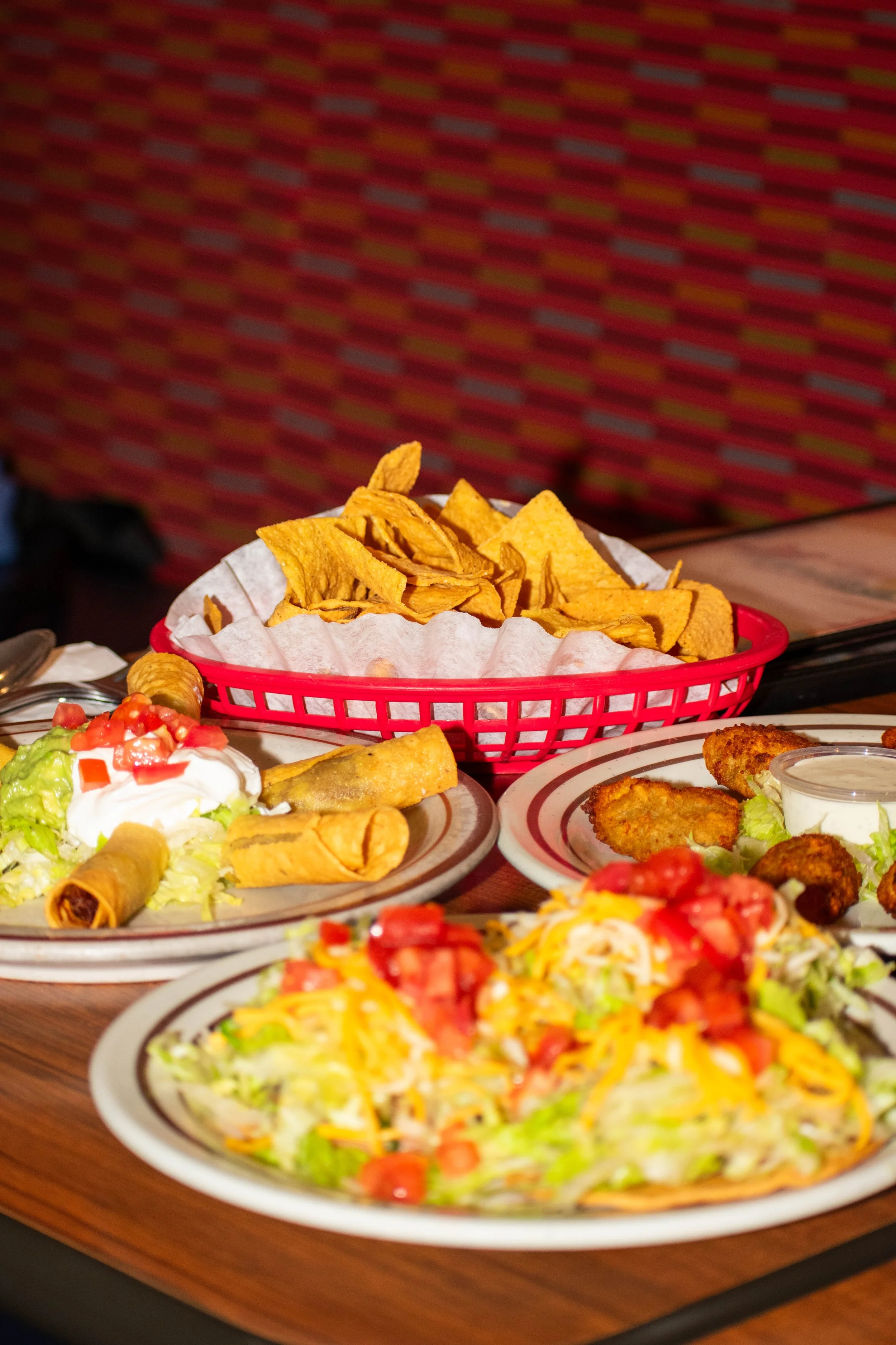 Assorted Mexican dishes including tacos, nachos, and salads on a wooden table.