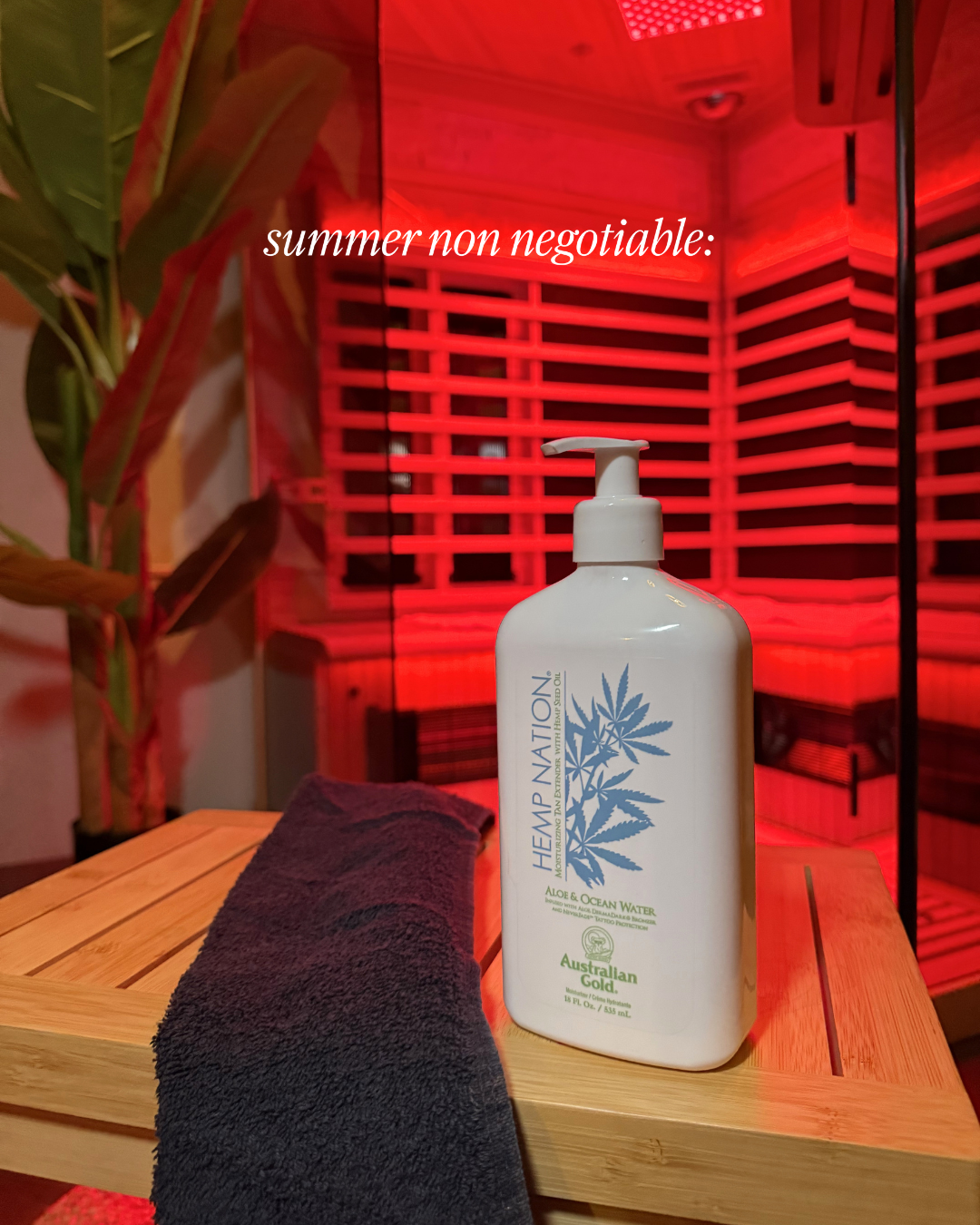 A bottle of hemp lotion labeled 'HEMP NATION Aloe & Ocean Water' on a wooden table, with a dark towel partially covering the table. In the background, a sauna with red lighting and wooden slats, and a potted plant are visible.