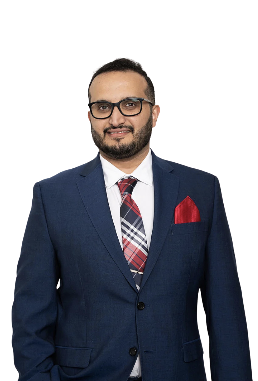 A man wearing glasses, a navy blue suit, a white dress shirt, a plaid tie, and a red pocket square, standing against a plain white background.