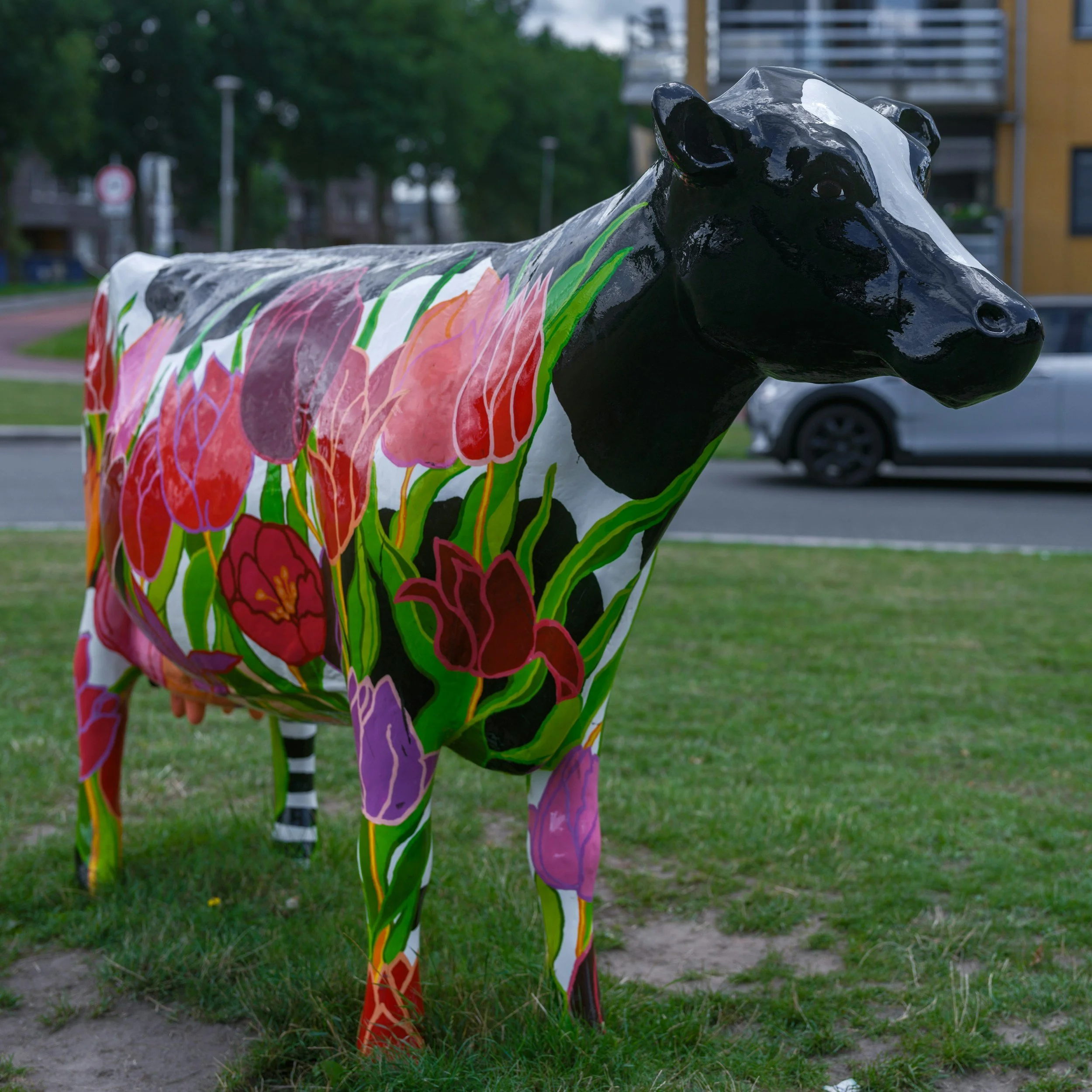 Colorful painted horse sculpture with floral patterns in an outdoor park setting with grass, trees, and buildings in the background.