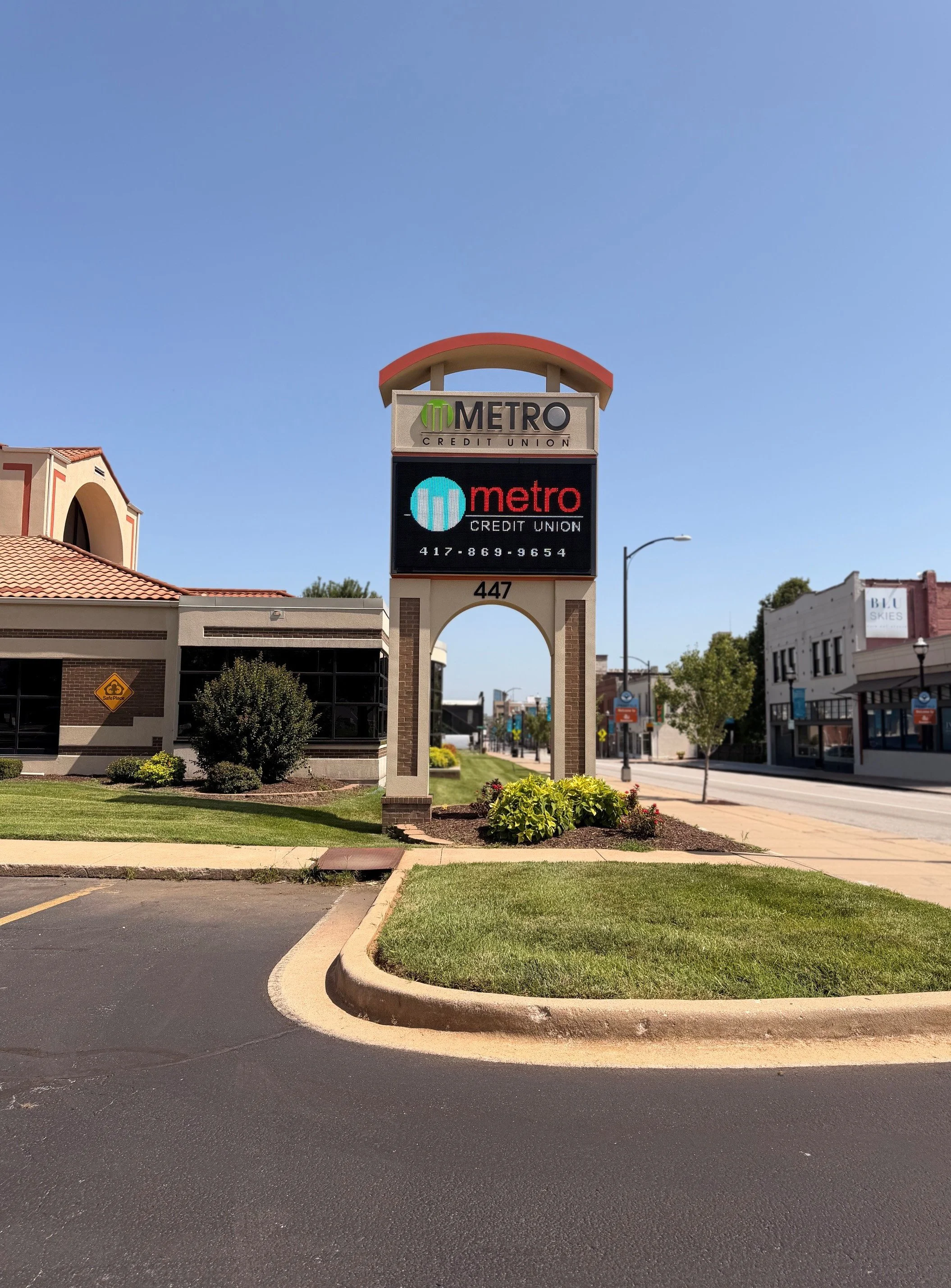 Street view with a sign for Metro Credit Union, buildings on both sides, sidewalk, street, and a blue sky.