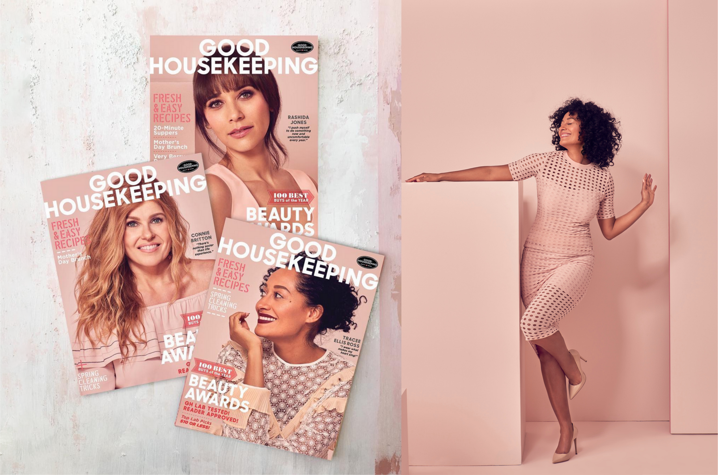 Multiple copies of "Good Housekeeping" magazine with various women featured on the covers, placed on a white wooden surface. To the right, a woman with curly dark hair wearing a beige polka dot dress poses against a pink wall.