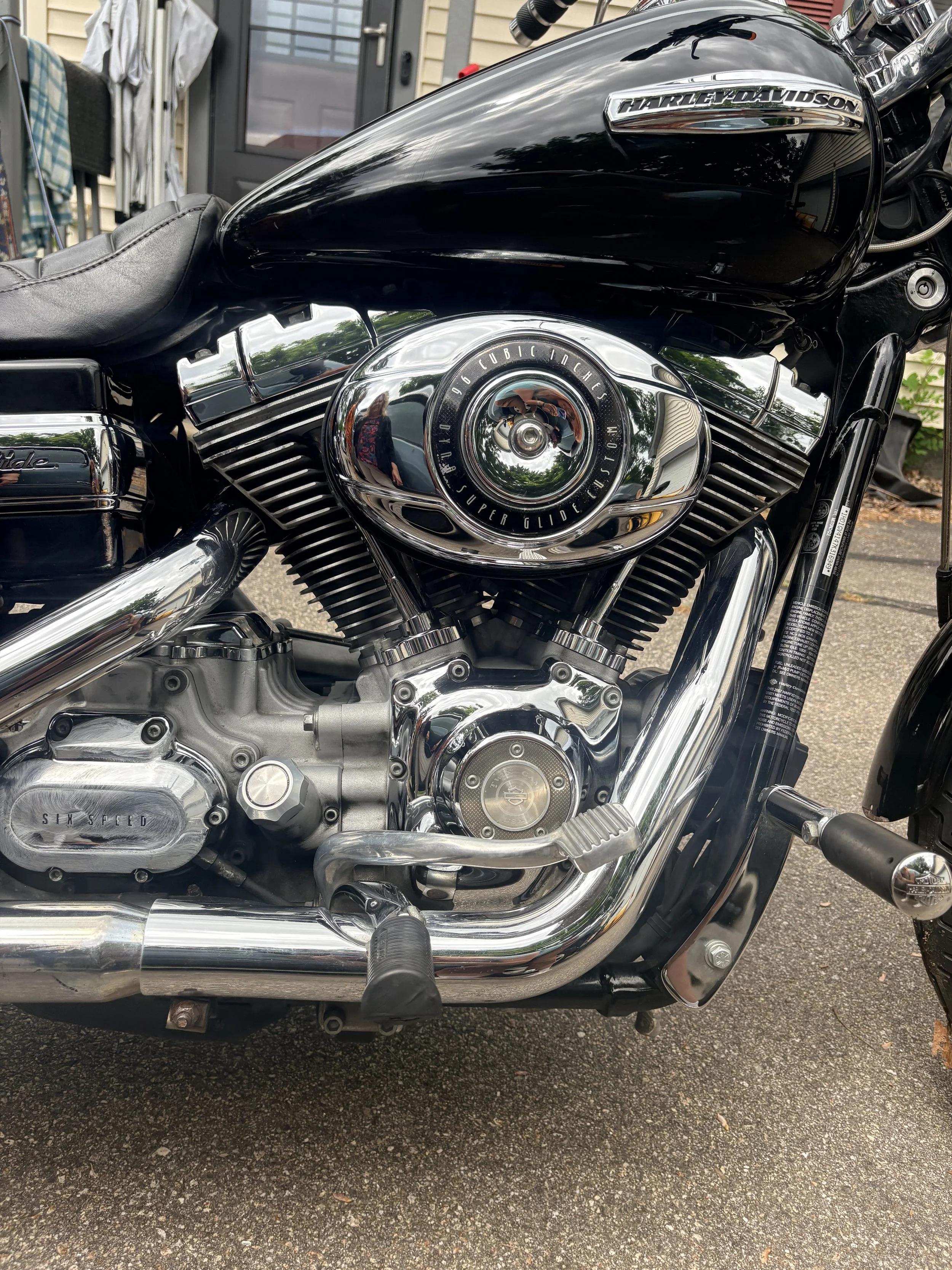 Close-up of a black Harley-Davidson motorcycle's engine and fuel tank, with chrome details and reflection of the surroundings on the chrome surfaces.