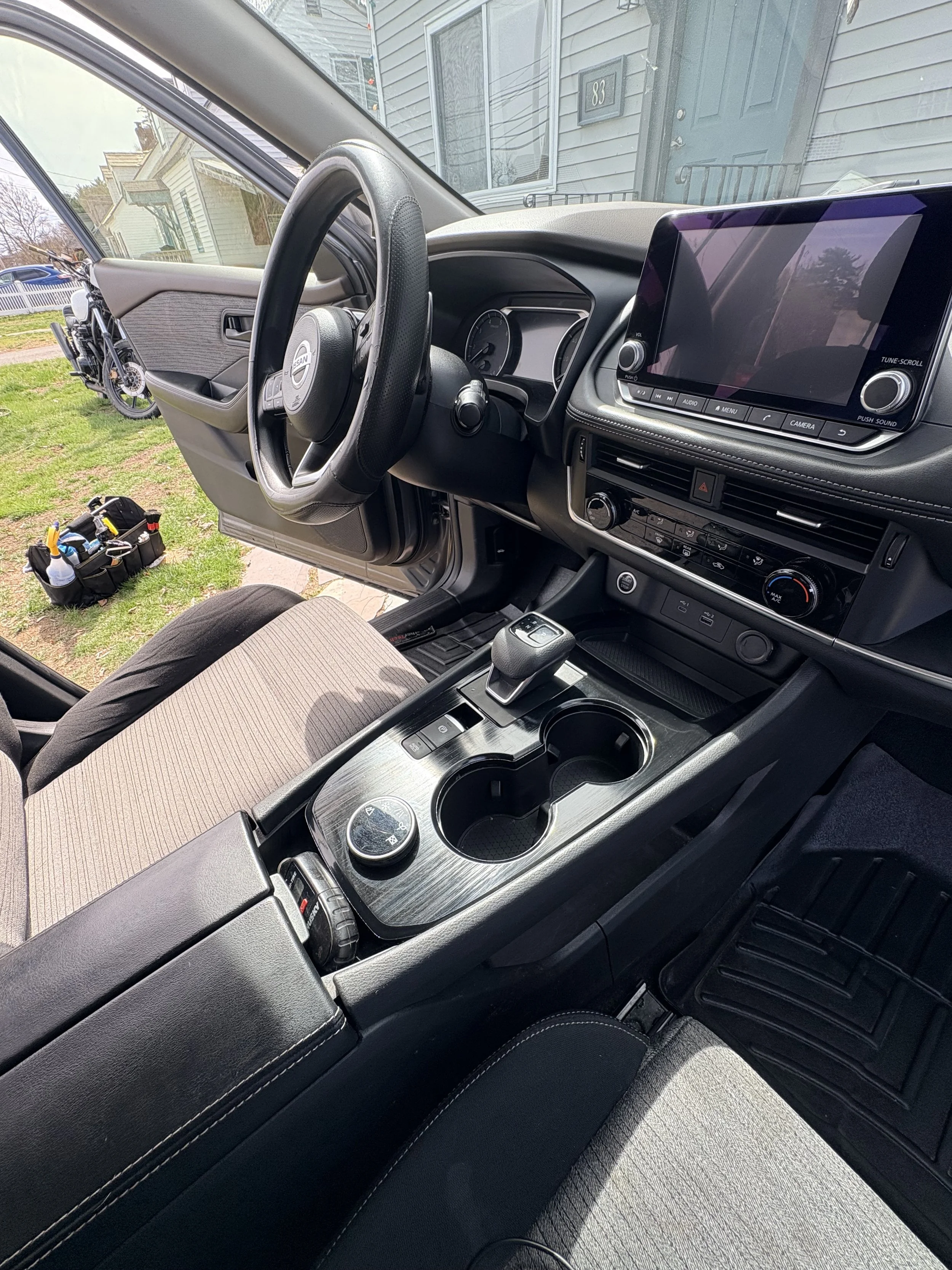 Inside a vehicle showing the dashboard, steering wheel, center console with gear shift, climate controls, and touchscreen display, with the driver's seat and front passenger seat visible.