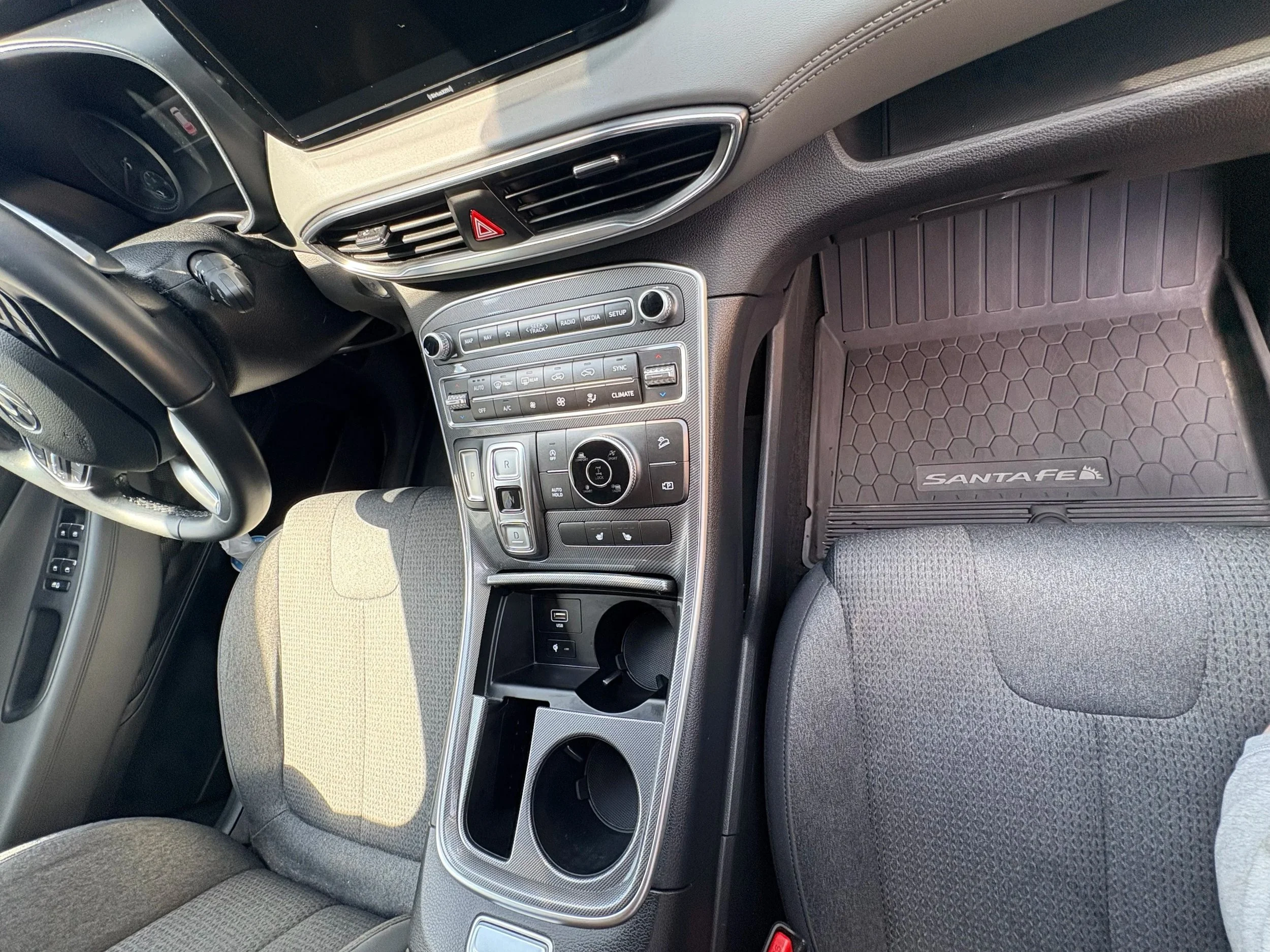 Inside view of a car's front interior, including the dashboard, steering wheel, center console with controls, and a black rubber floor mat with the brand name 'Santa Fe'.