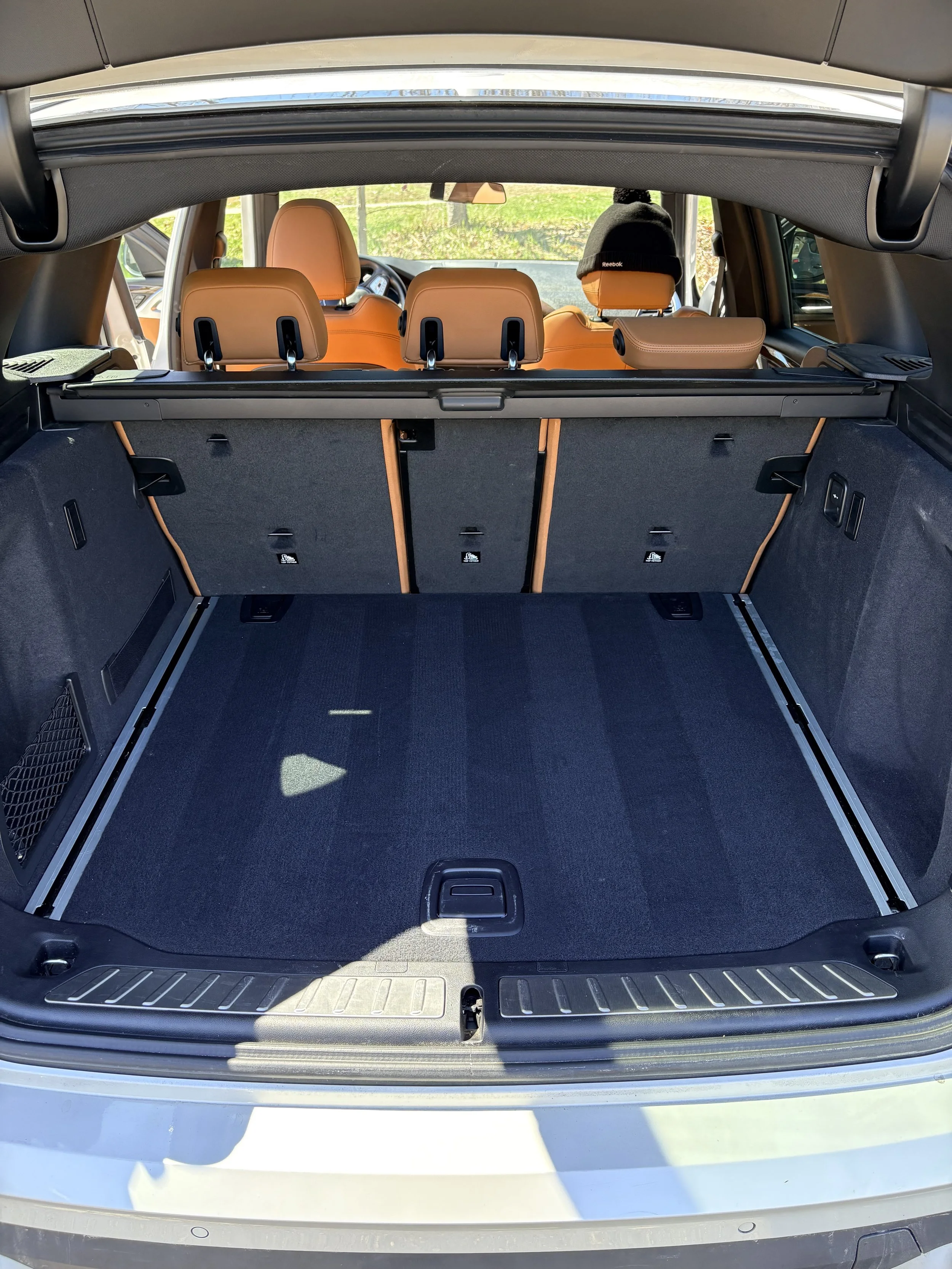 Empty car trunk showing the interior with beige seats and a view through the rear window of a green outdoor area.
