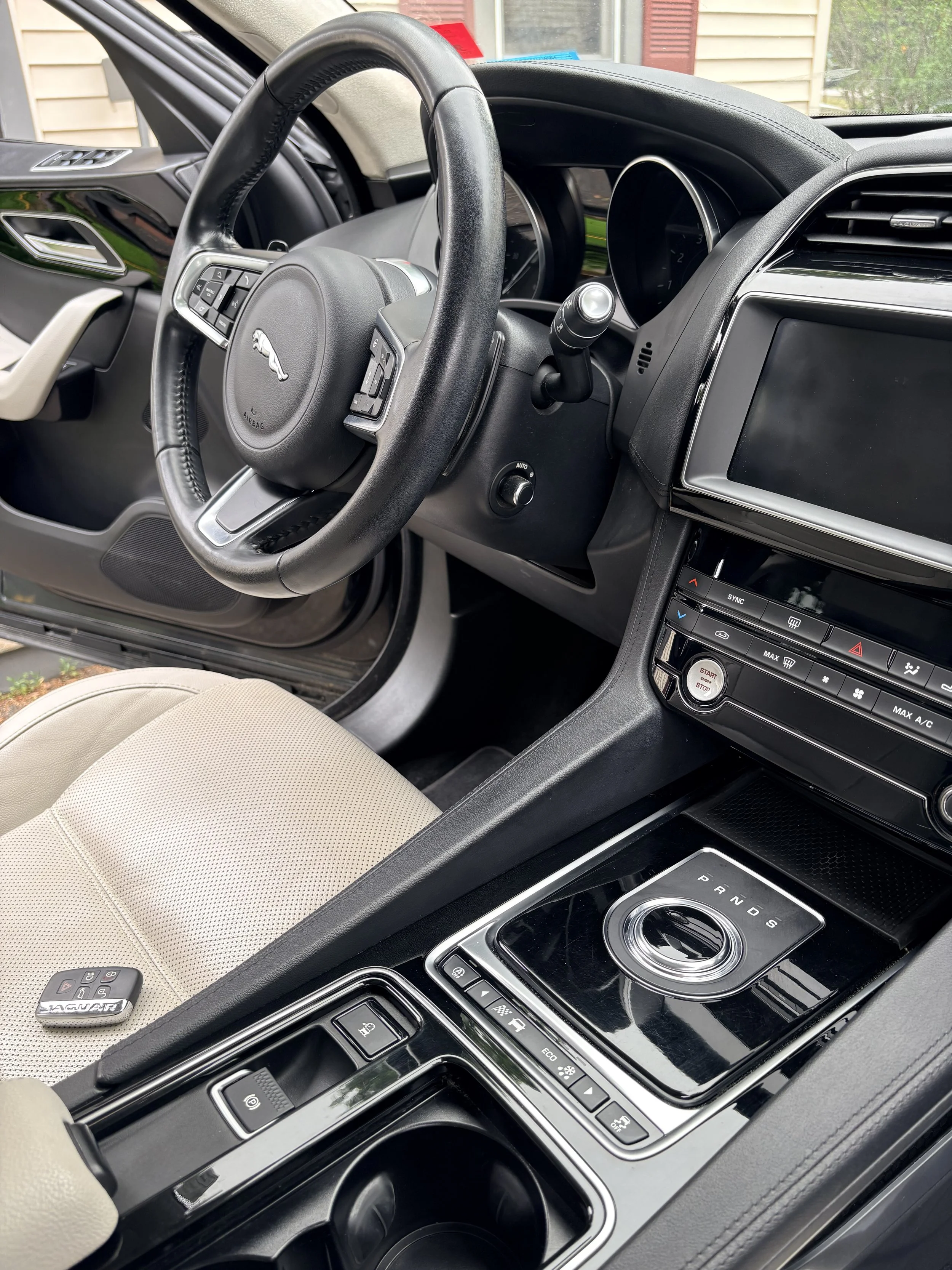 Interior view of a Jaguar vehicle showing the steering wheel, dashboard, center console with gear shift, and beige seats.