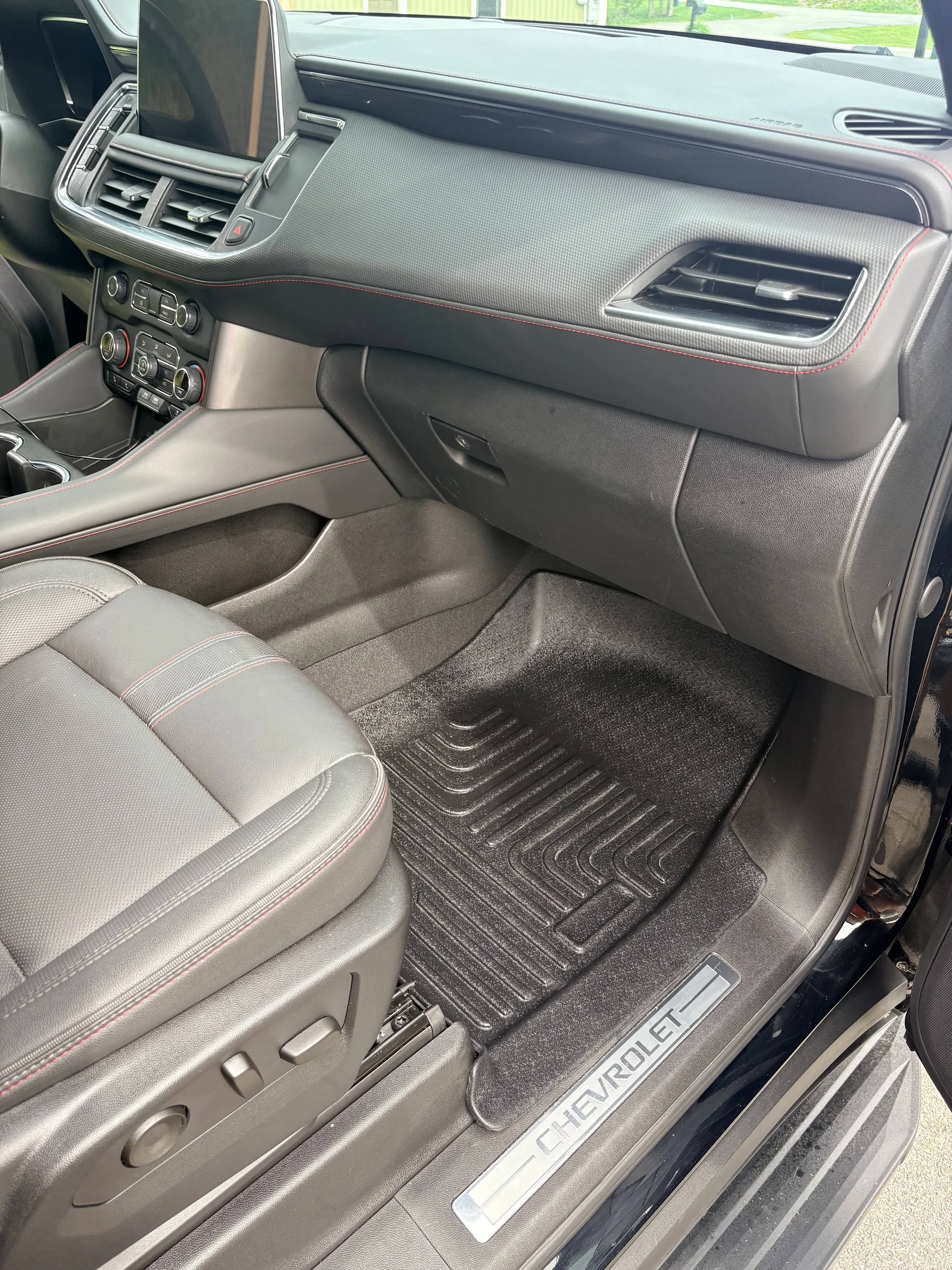 Front passenger side interior of a Chevrolet car, showing the dashboard, air vents, glove compartment, and part of the seat with red stitching, along with the Chevrolet-branded door sill.