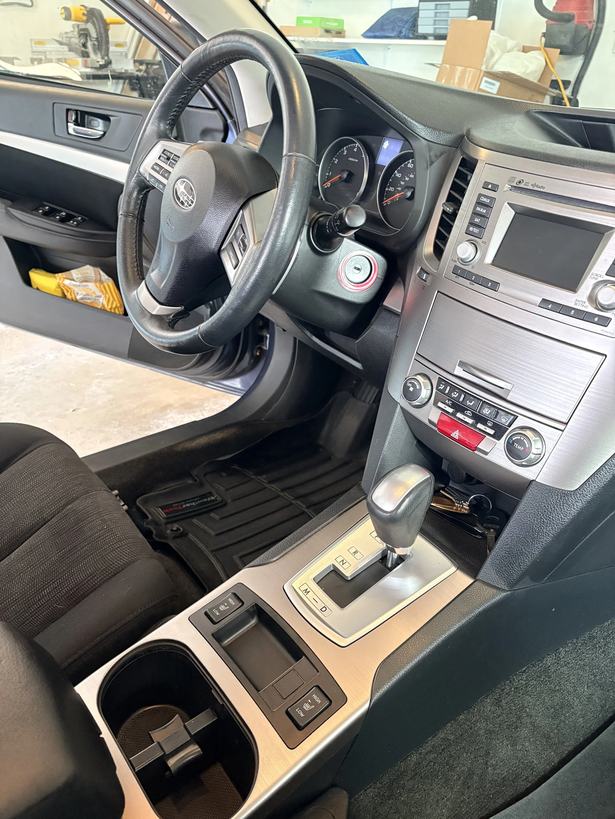 The interior of a car, showing the steering wheel, dashboard with speedometer and other controls, gear shift, and center console with buttons and a screen.