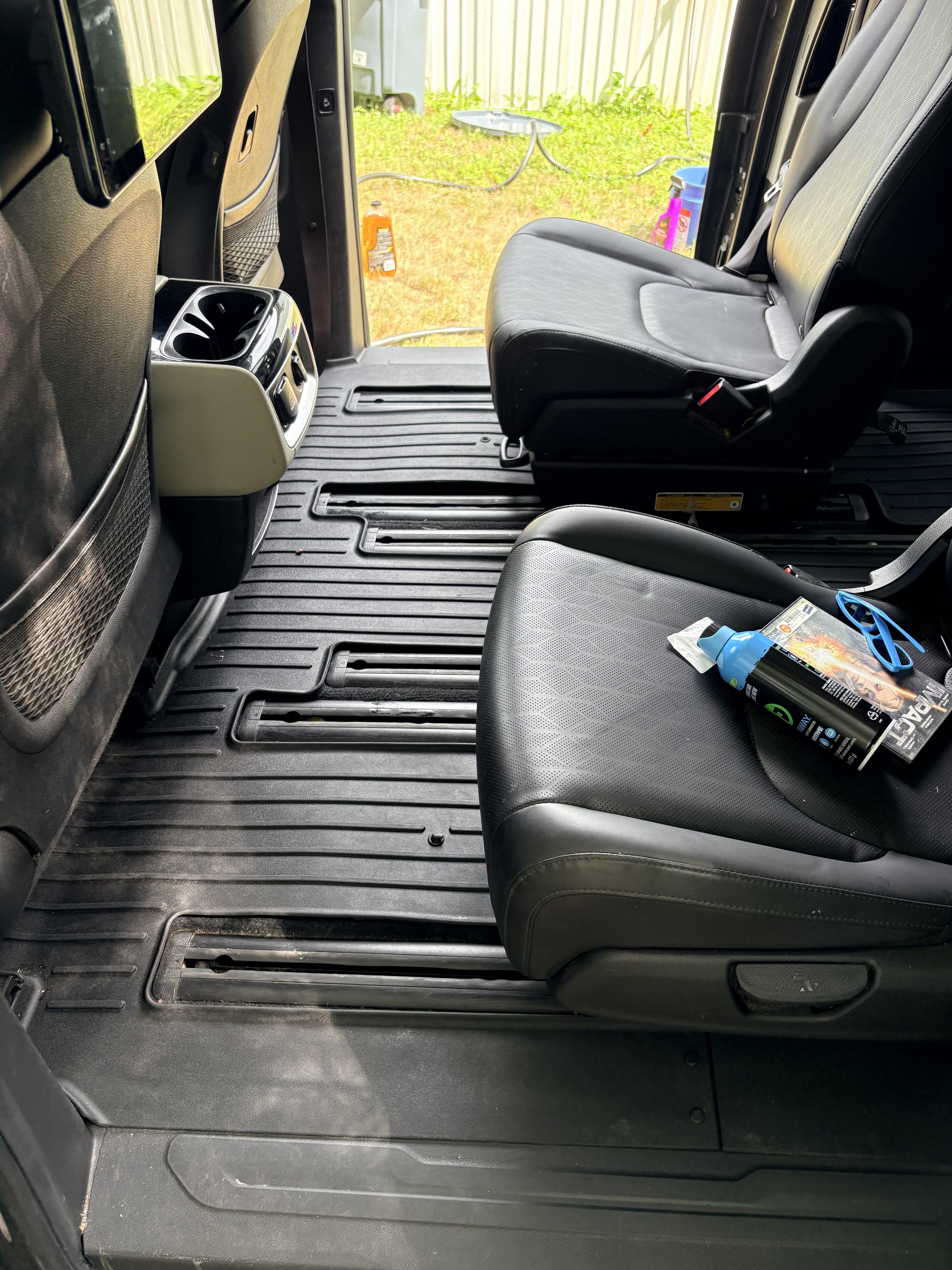 View of the interior of a bus, showing two black seats, a floor mat, and a view outside through an open door with grass, a fence, and some outdoor items.