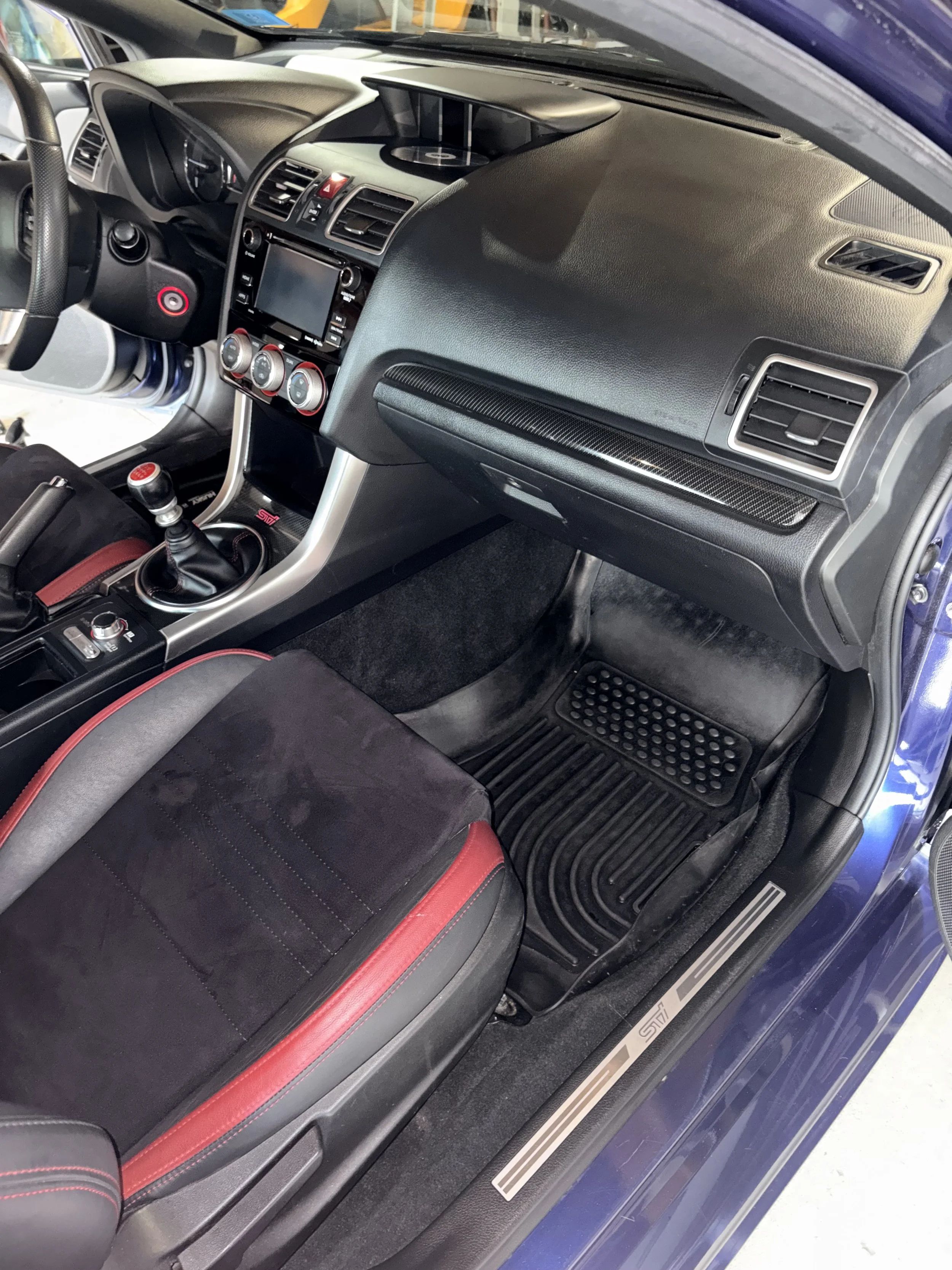 The interior of a sports car with a black dashboard, touchscreen display, air vents, red and black seats, and a manual gear shift lever.