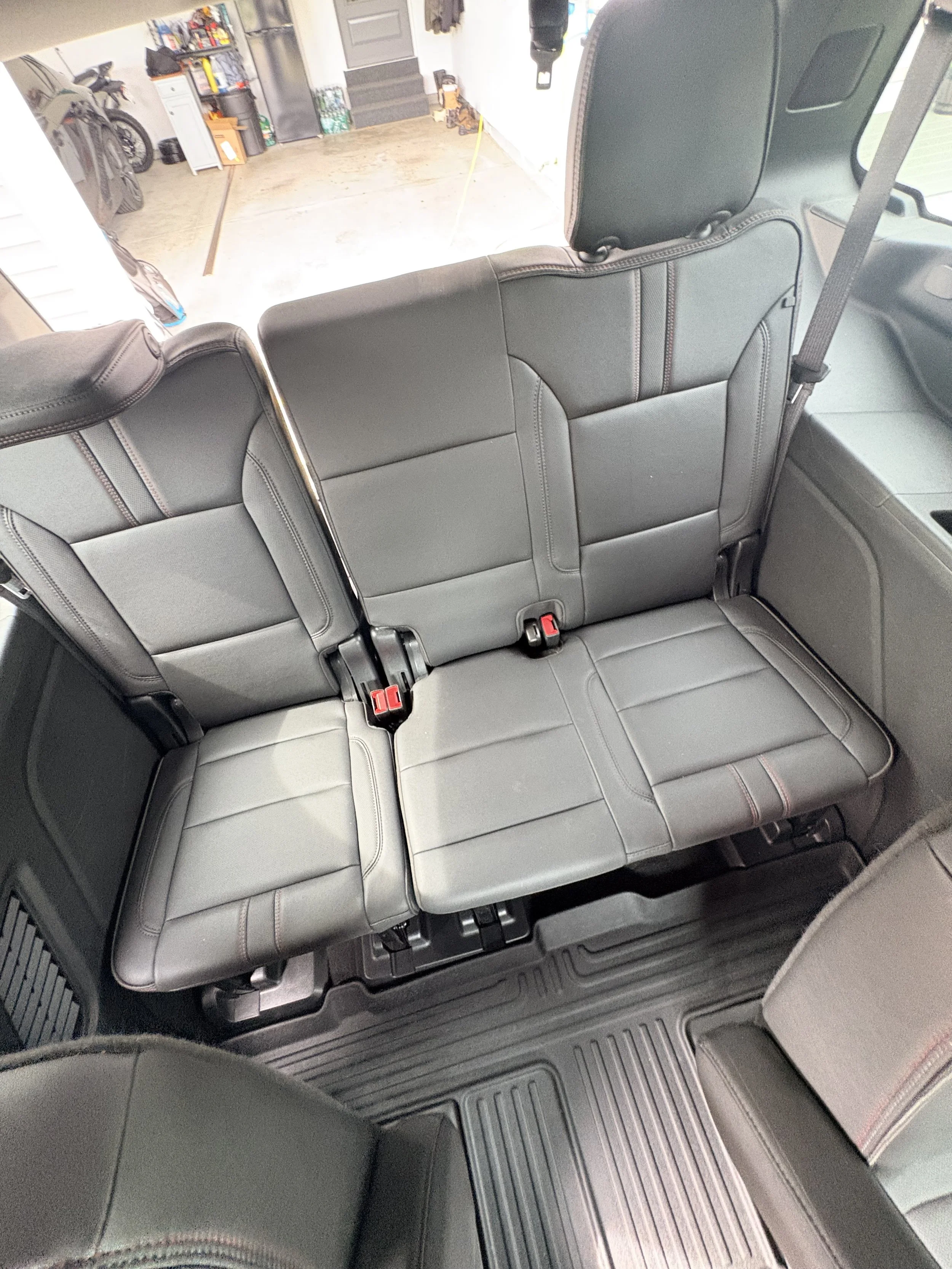 The interior of a vehicle showing gray leather seats, with an adult seat in the foreground and several child booster seats in the back. The vehicle is parked in a garage with concrete flooring, tools, and a bicycle visible in the background.
