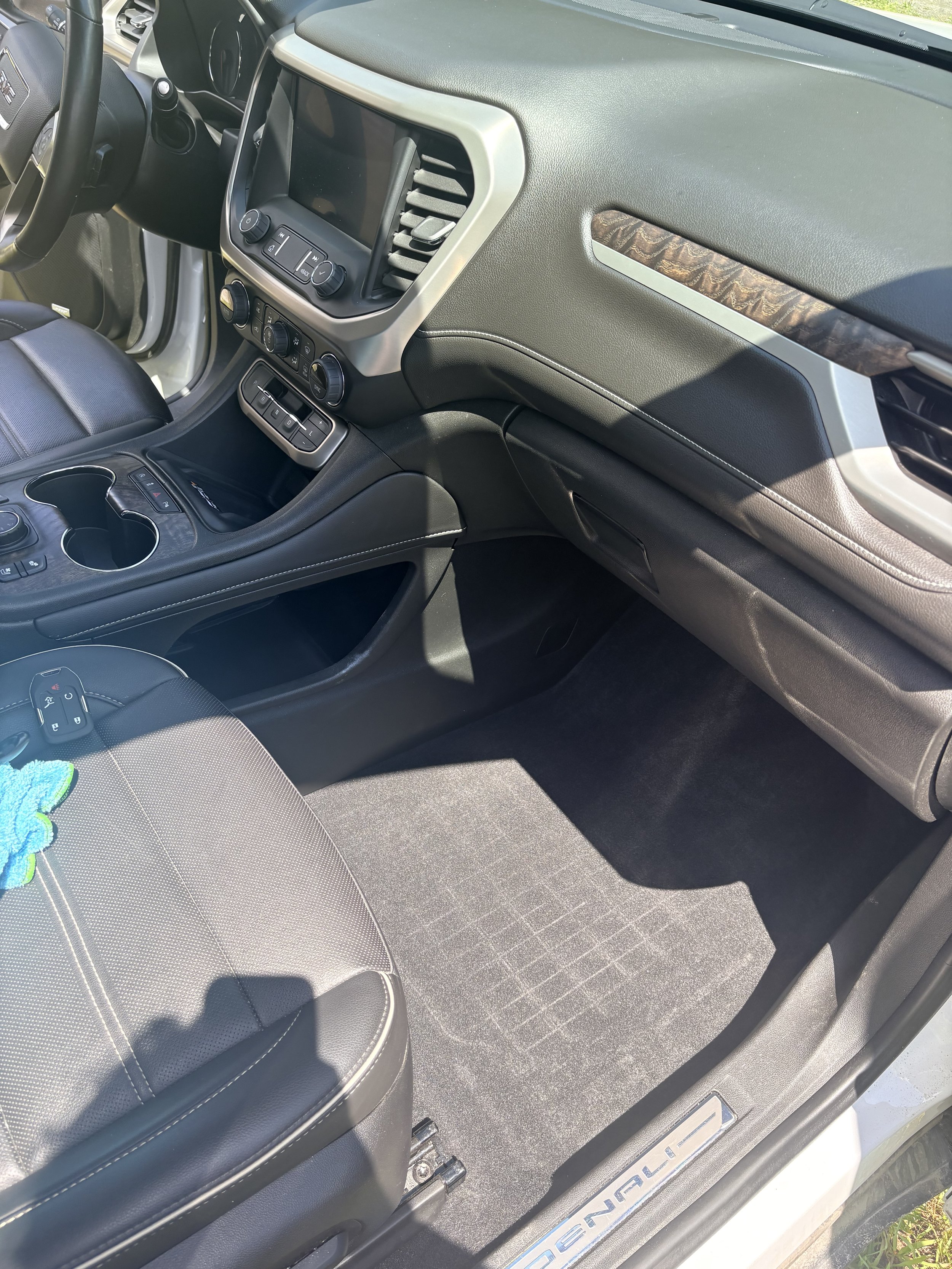 The interior of a vehicle showing the passenger side dashboard, black leather seat, and floor mat with the word 'DENALI' on a metallic plate.