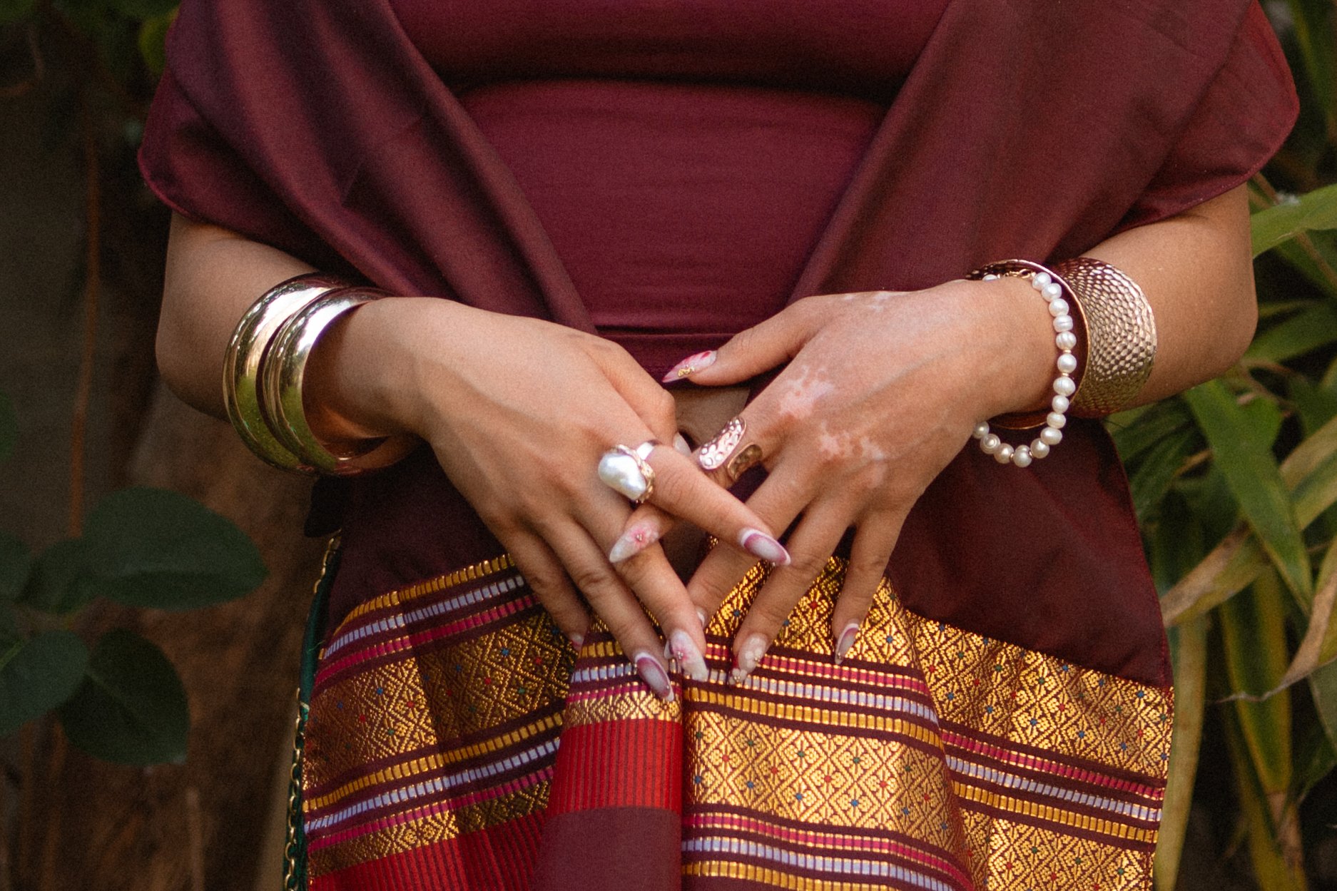 Frau trägt traditionelle philippinische Kleidung mit zahlreichen Schmuckstücken, darunter Armreifen, Ringe, eine Perlenkette und ein Geflecht aus Golddraht, in einem natürlichen Umfeld.