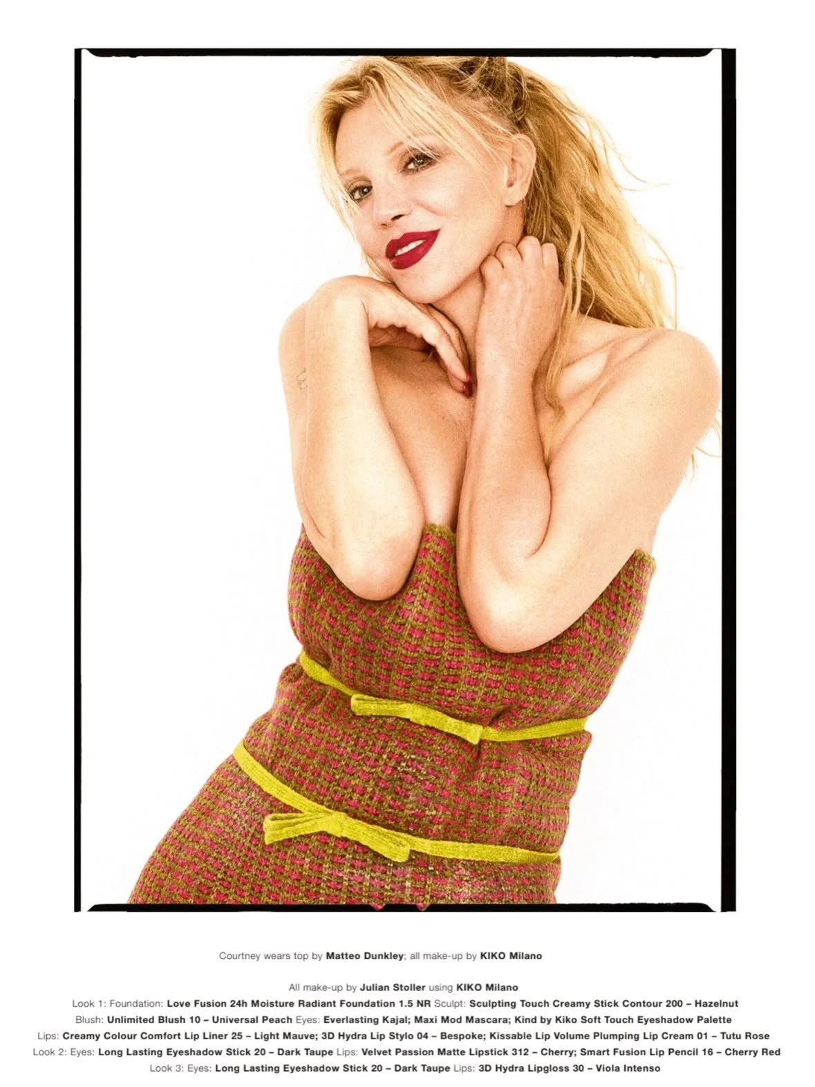 Portrait of a woman with blonde hair, red lipstick, posing with her hands near her neck, wearing a colorful textured dress with yellow accents.