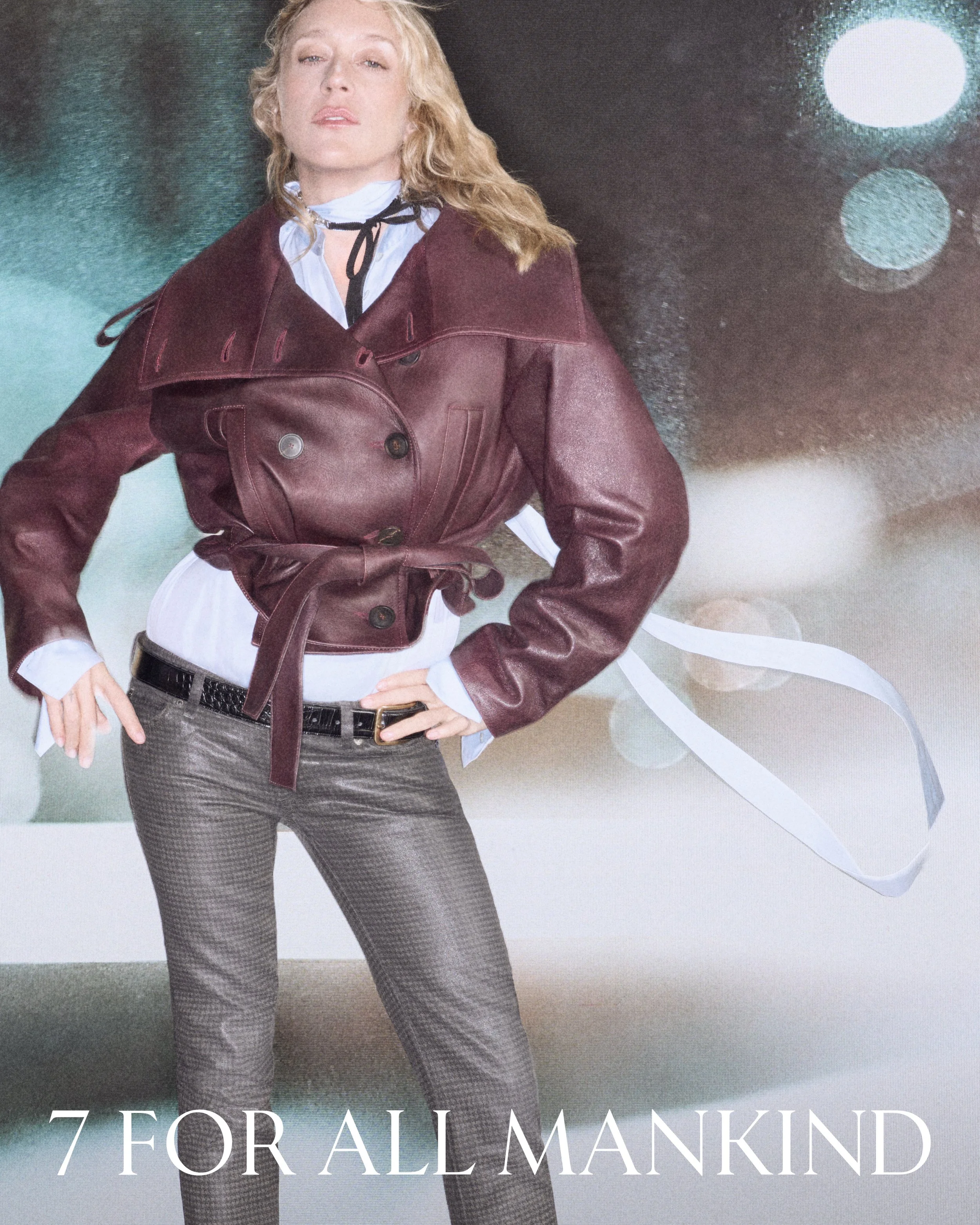 Poster of a woman in a maroon leather jacket over a white blouse, wearing patterned pants and a black belt, with her hand on her hip, against a dark and colorful abstract background with circles of light.
