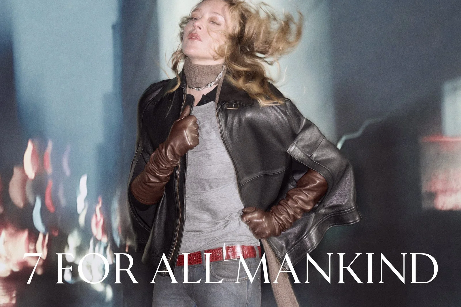 A woman with blonde hair is in a city at night, wearing a leather jacket and brown gloves, with a confident pose. The text overlay reads '7 for All Mankind'.