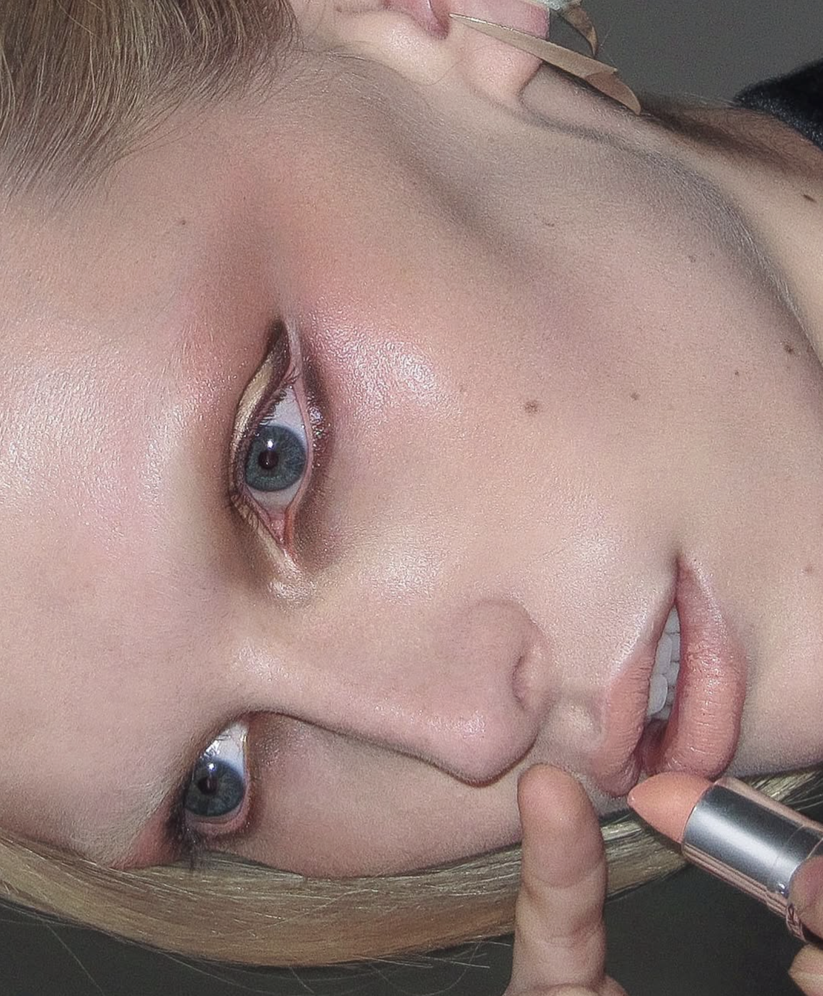 A close-up of a woman with makeup, touching her face with her fingers, showing her eye, makeup, and part of her nose and mouth.