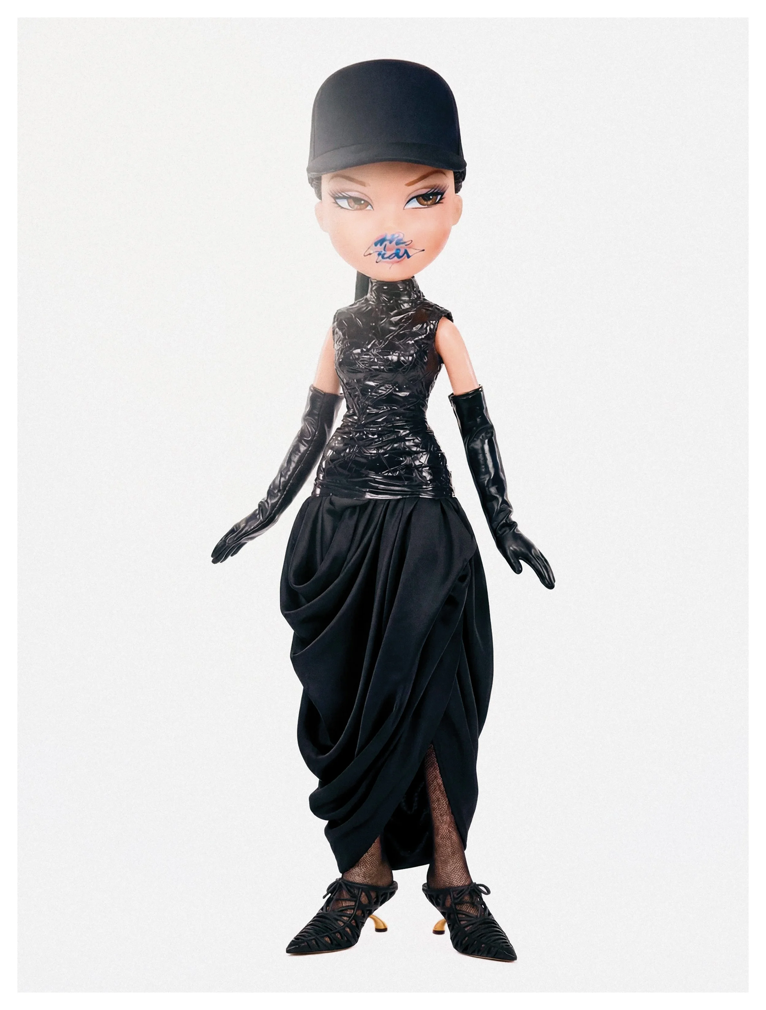 A fashion doll with a stylized face, wearing a black cap, a shiny black sleeveless top, long black gloves, a big black skirt, fishnet stockings, and black high-heeled shoes with laces, posed against a plain light background.