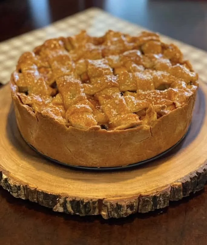 Apple pie with a golden crust and caramelized apple filling on a wooden slice serving board.