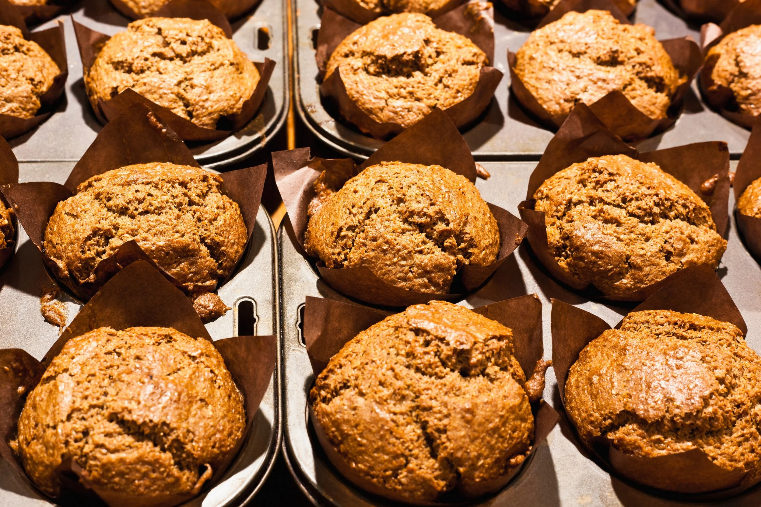 A tray of freshly baked pumpkin muffins in brown paper baking cups.