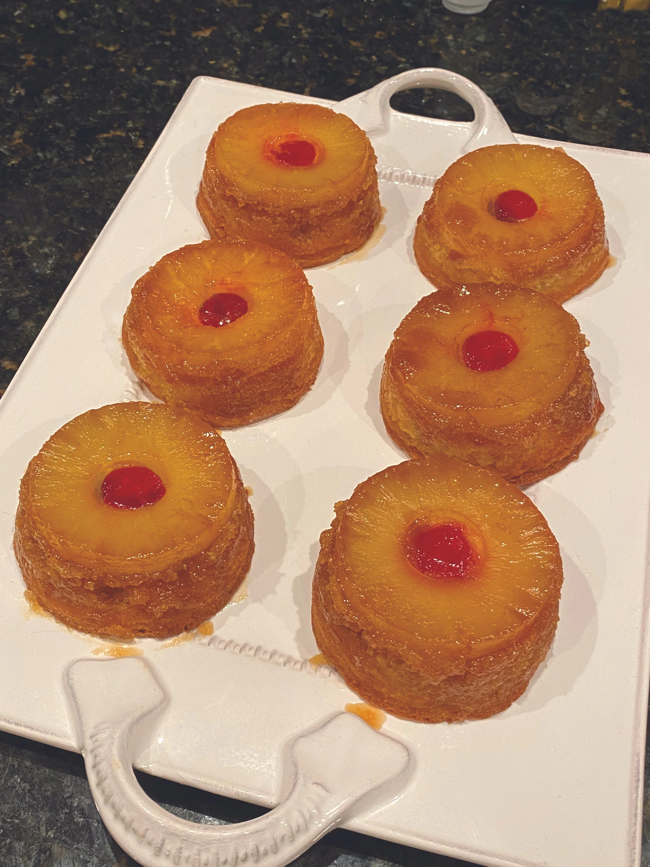 Four pineapple upside-down cakes with cherries on top arranged on a white serving tray.