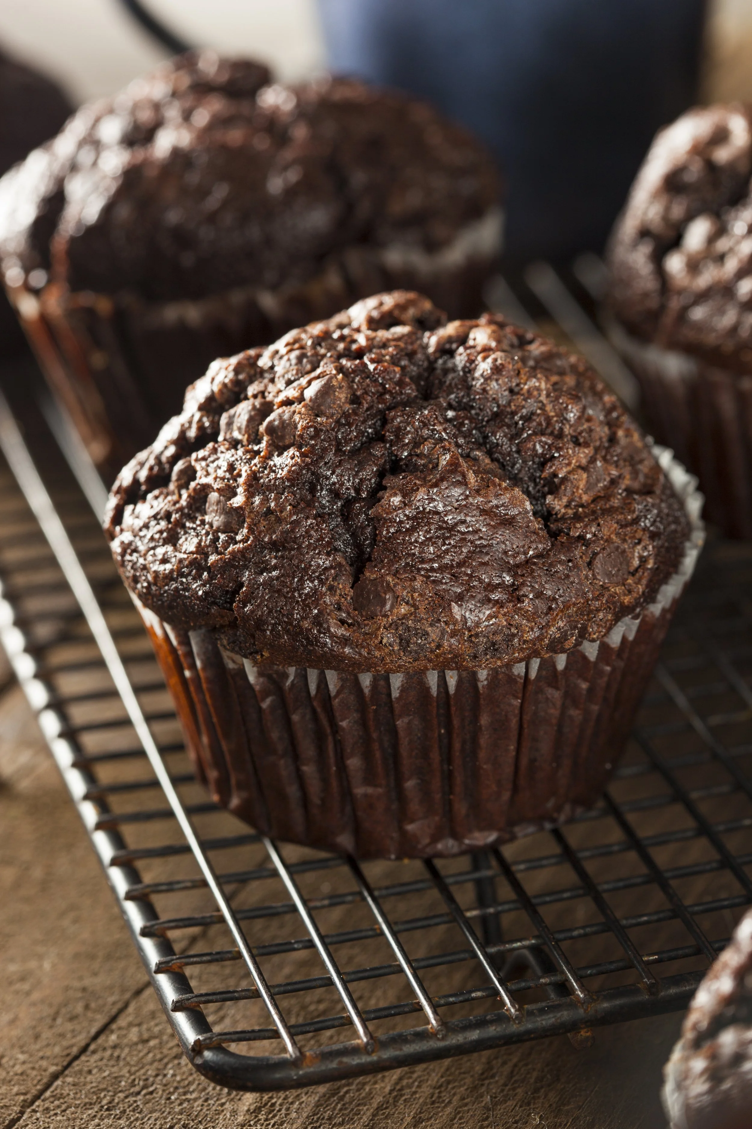 Close-up of a freshly baked double chocolate muffin on a wire rack, with other muffins blurred in the background.